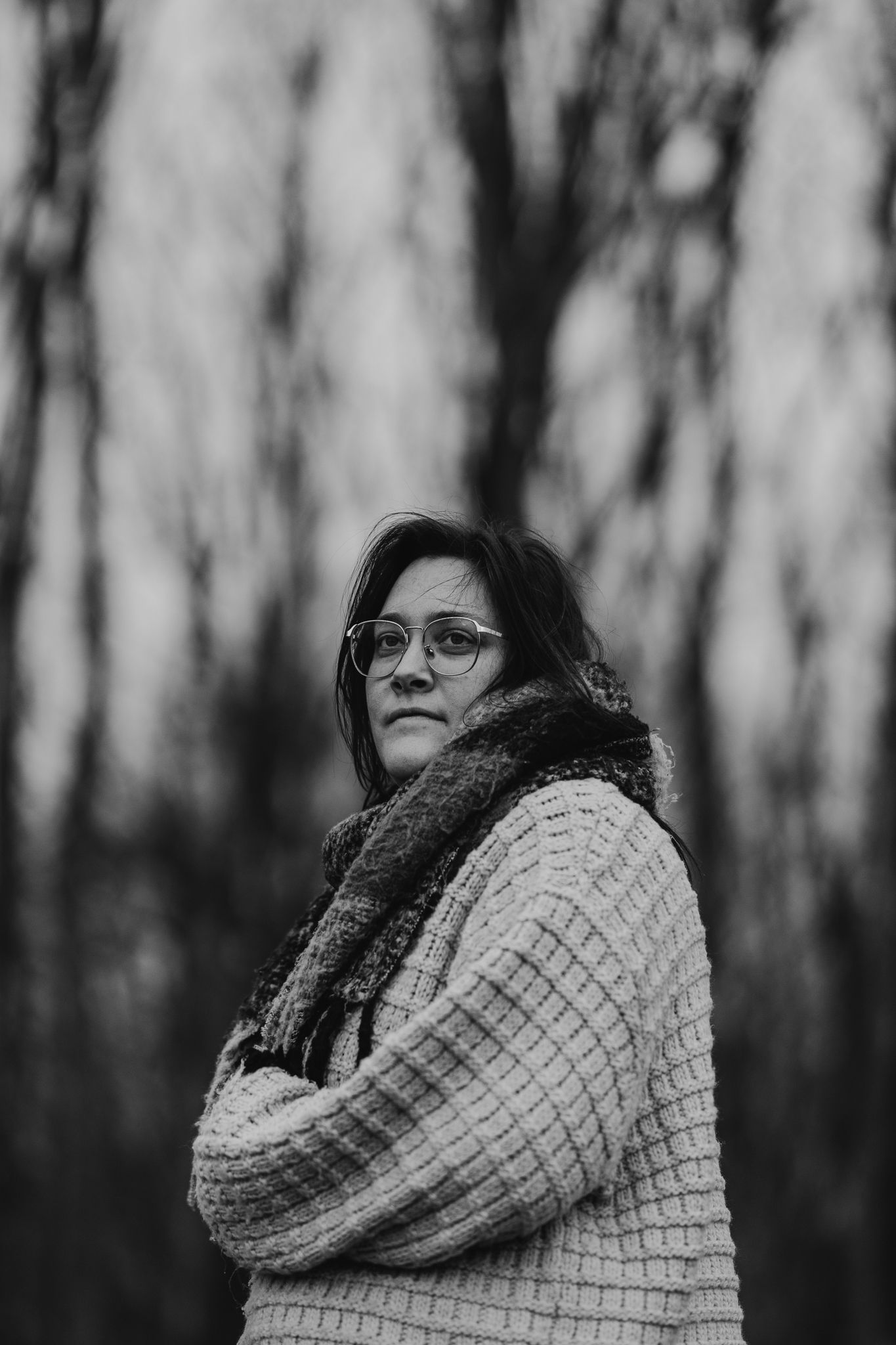 Woman in glasses and scarf posing outdoors in black and white winter portrait.