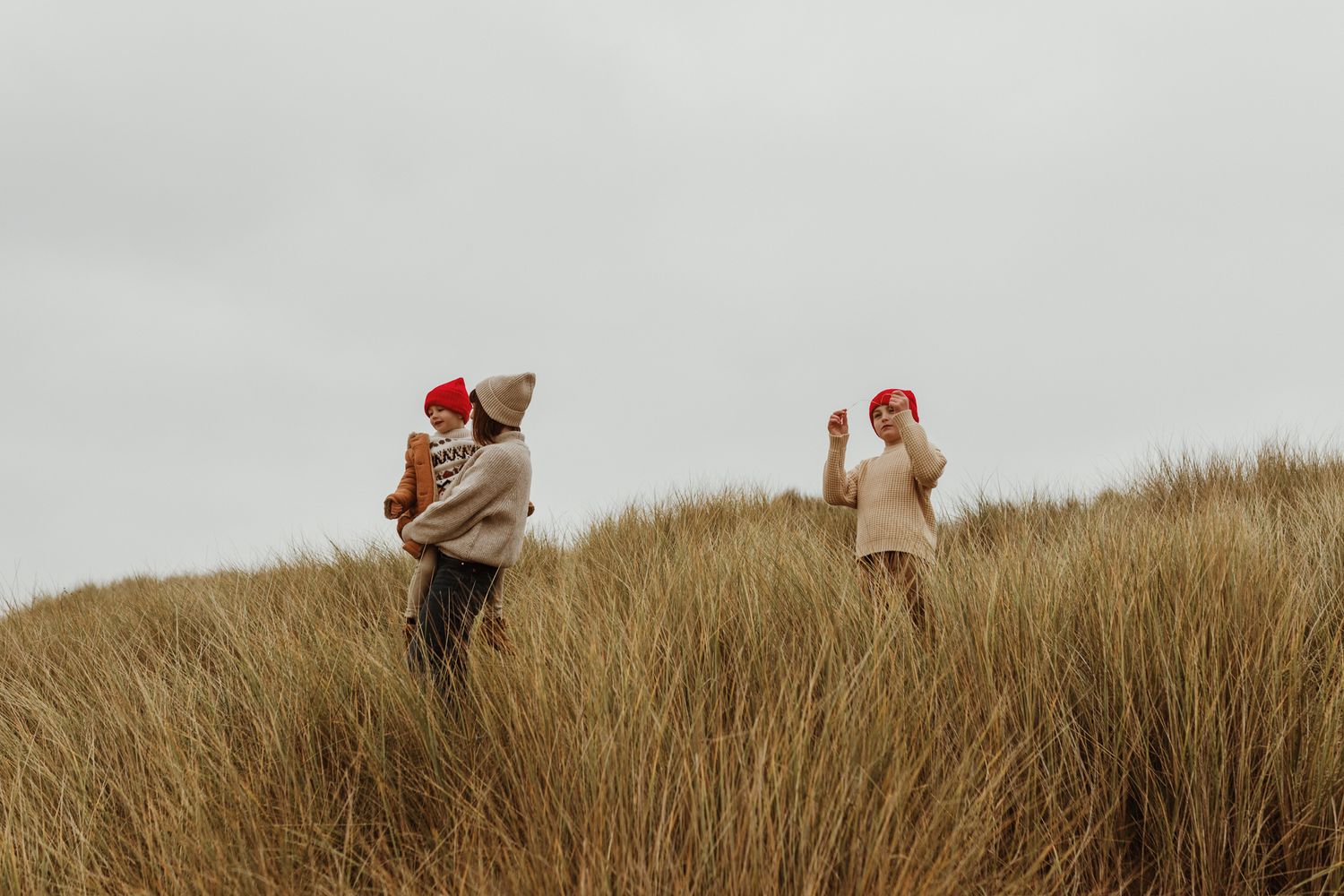 Two people in matching red hats standing in tall grass dunes on overcast day.
