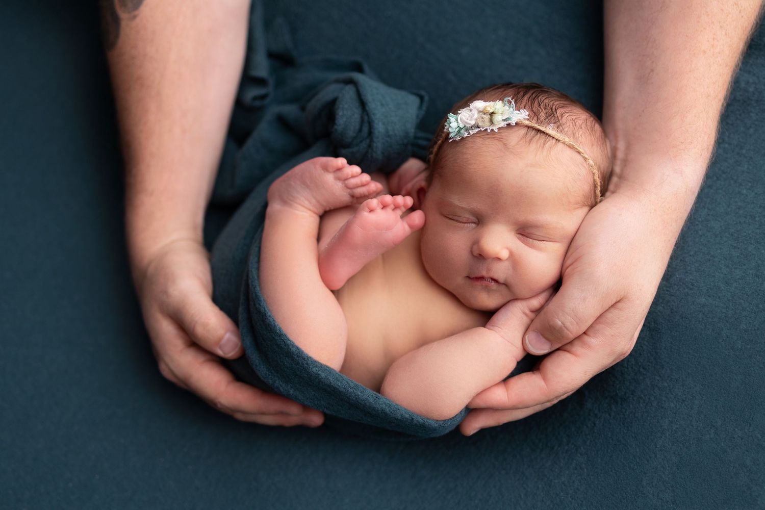 Newborn baby wrapped in blue fabric cradled in parents hands, soft studio photography in Vacaville California
