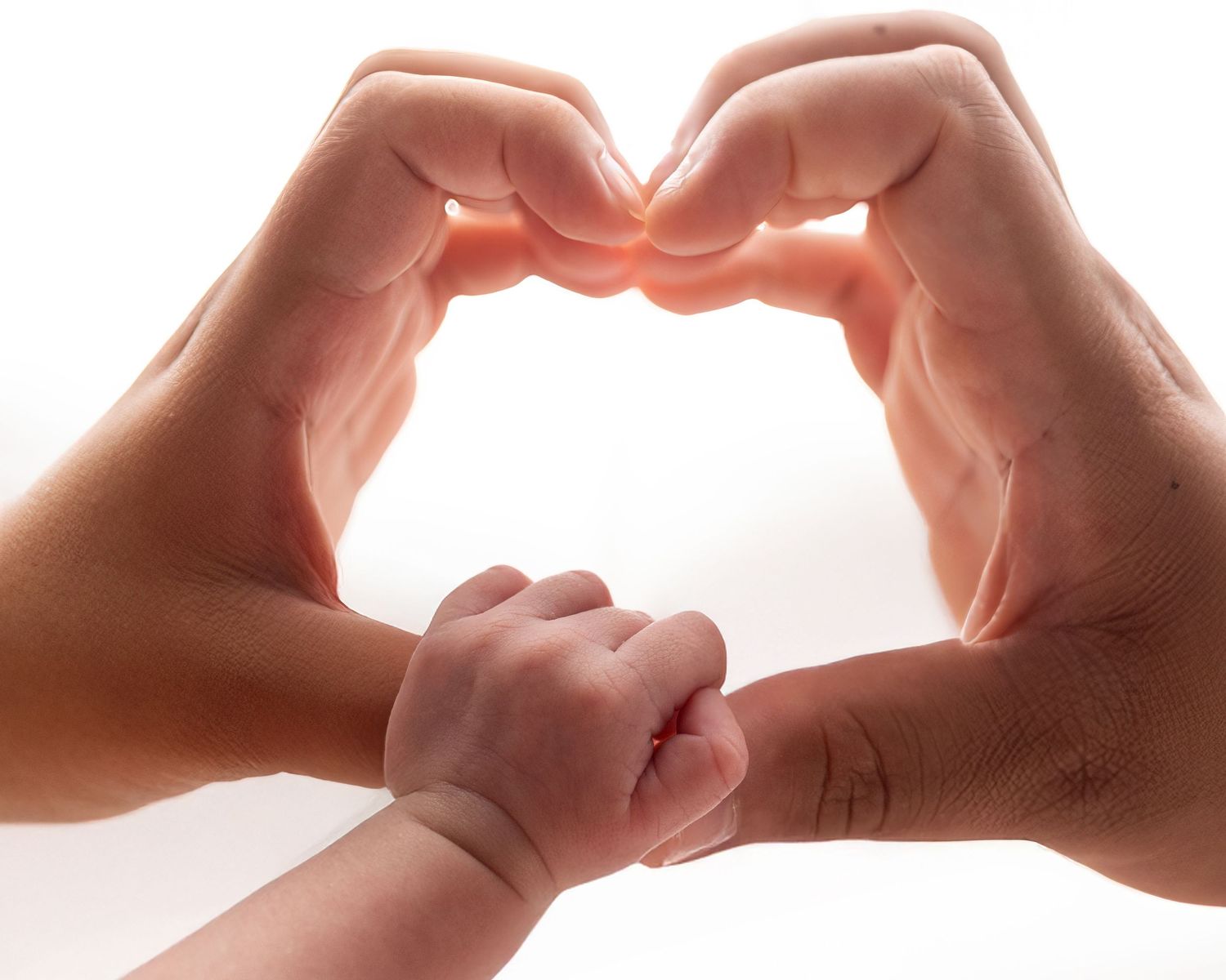 Two adult hands forming a heart shape with a small baby hand reaching through the center on white background.