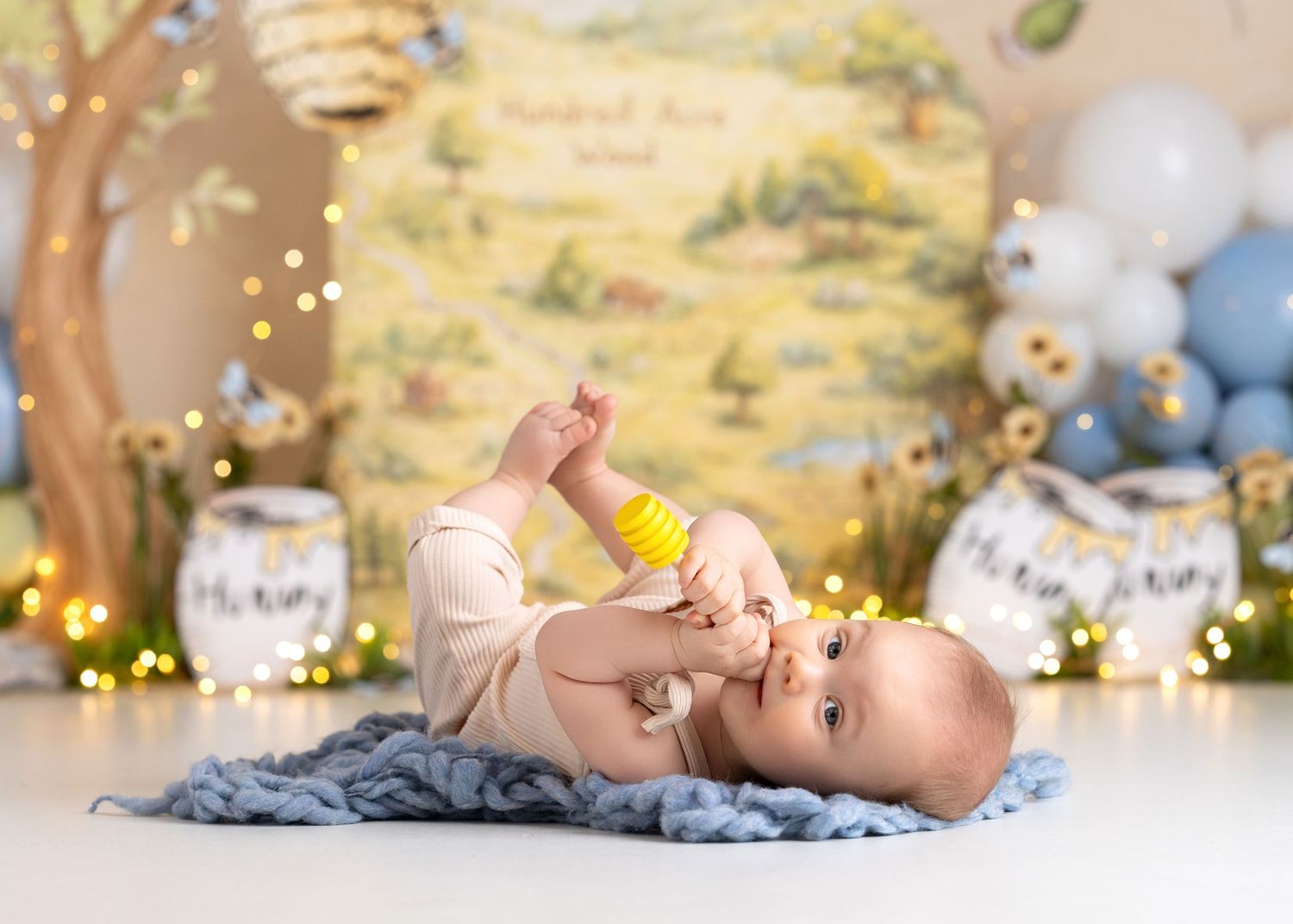 winnie the pooh theme, Baby lying on blue blanket chewing yellow toy with Winnie the Pooh backdrop and bokeh lights.