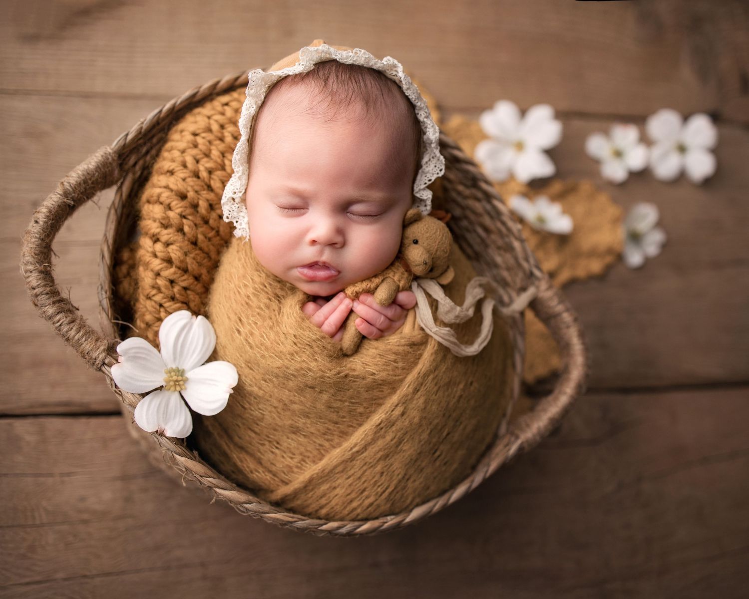 Sleeping newborn baby in a wicker basket wrapped in golden knit, wearing a lace bonnet, holding a tiny bear.