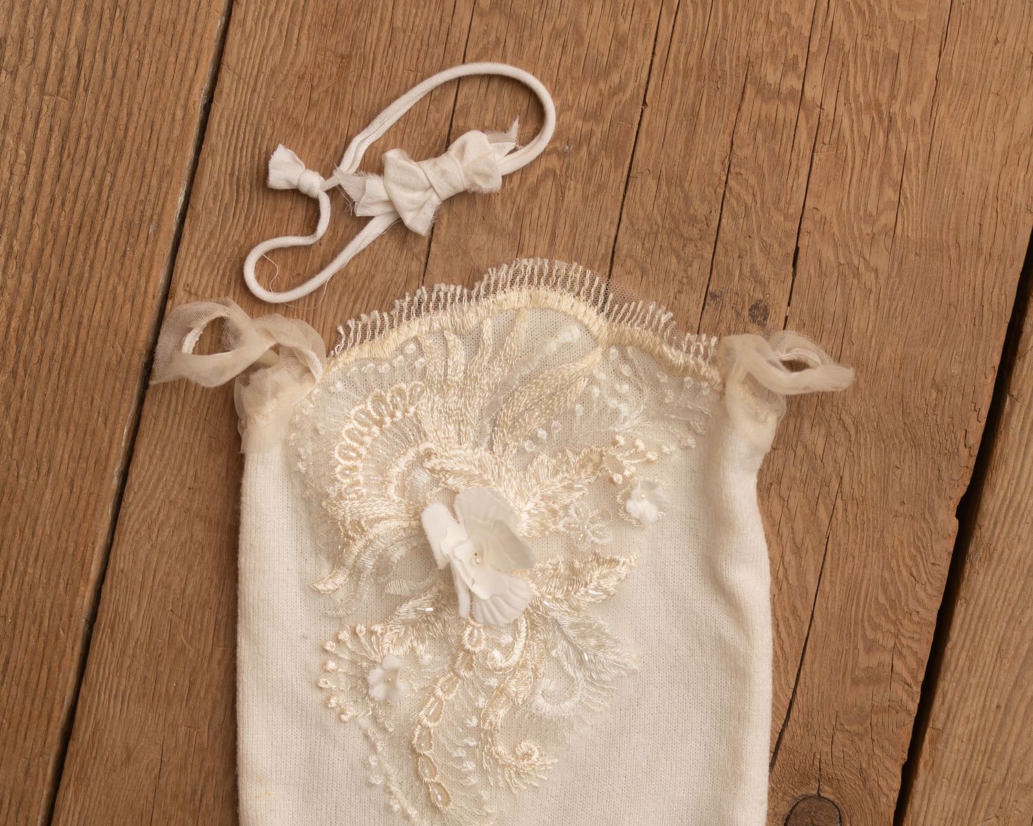 Delicate ivory lace newborn romper with floral embroidery and matching headband on rustic wood background.
