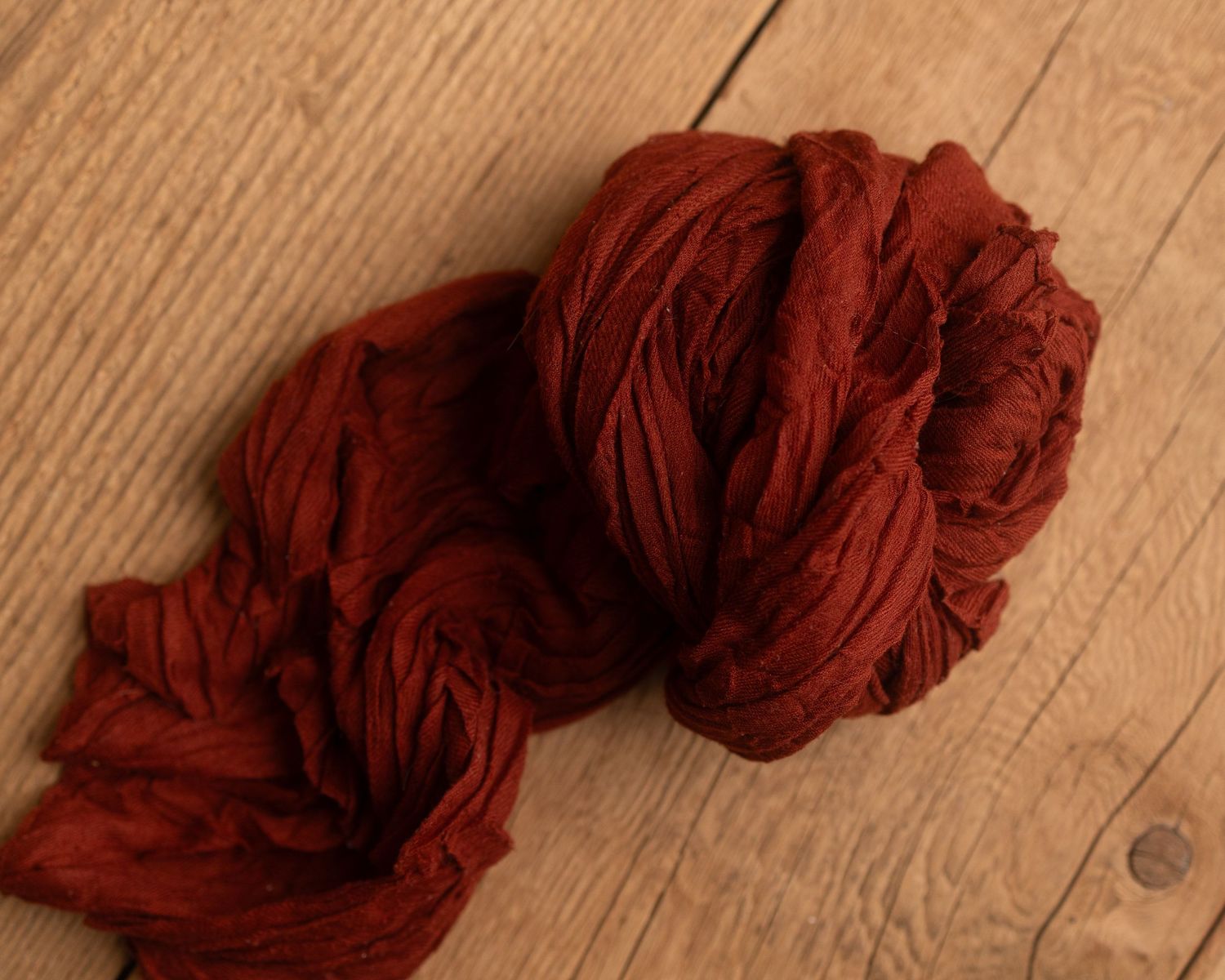 A rustic red-brown yarn skein resting on a wooden surface, perfect for knitting or weaving projects.