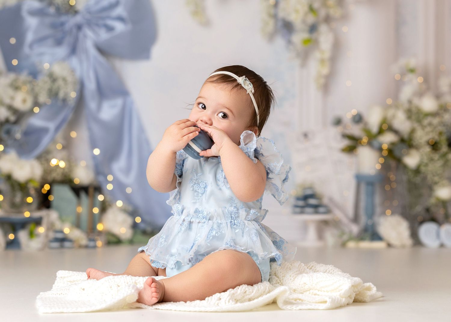 Bridgerton Theme, Baby girl in blue floral romper eating cake during first birthday cake smash photo session.