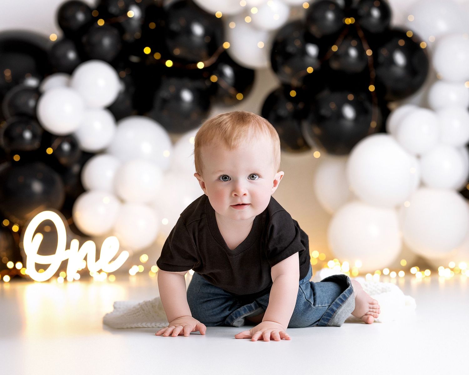 Baby's first birthday cake smash with black and white balloons, fairy lights, and glowing One sign.