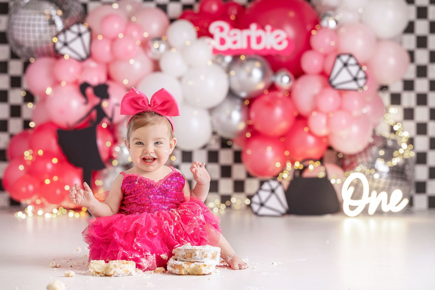 Baby girl celebrating first birthday with Barbie themed cake smash, pink balloon backdrop in Vacaville California