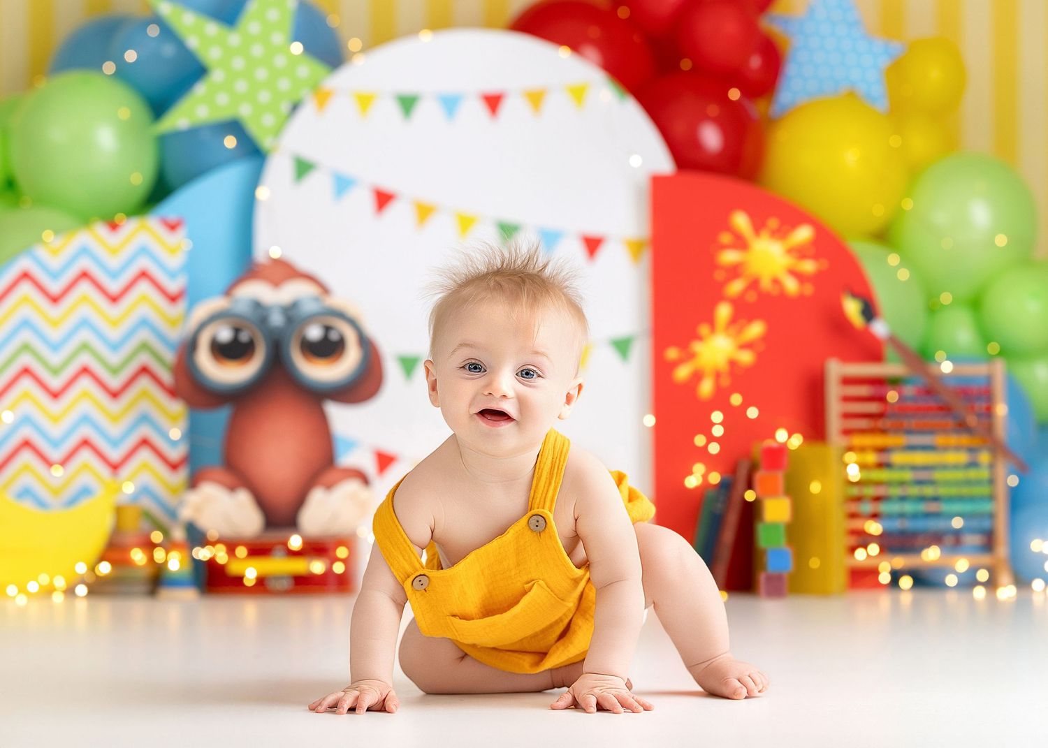 Baby in yellow romper smiles during colorful first birthday cake smash with balloons and festive decorations, Curious George theme.