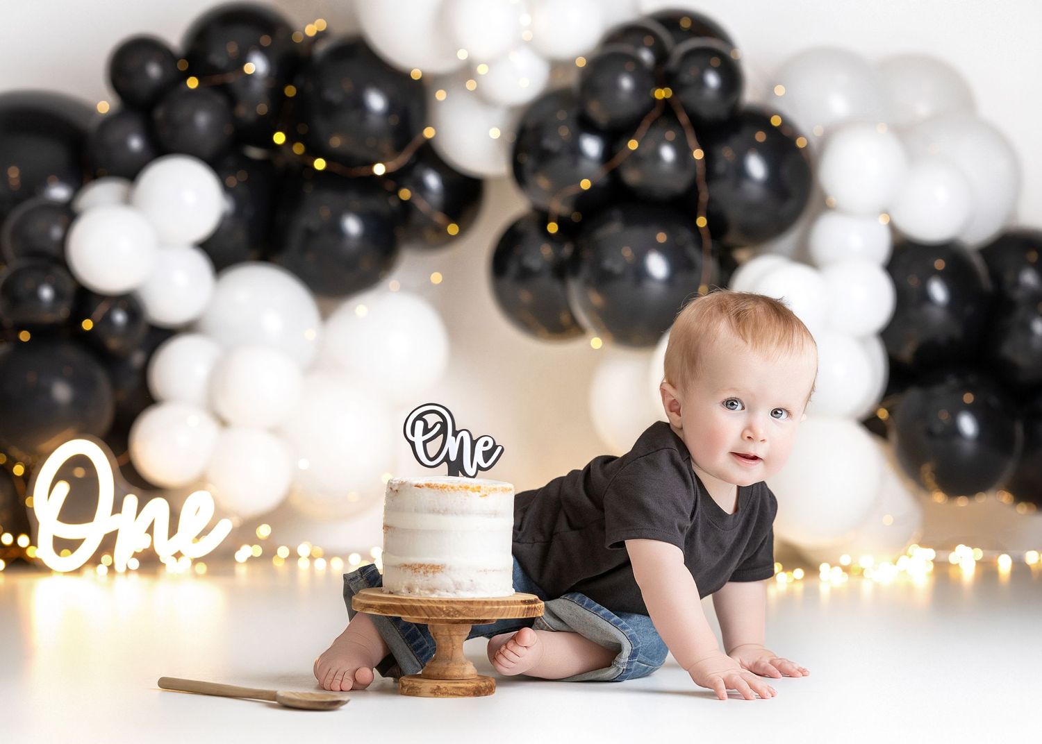 Baby's first birthday cake smash with black and white balloon garland, white cake with 'One' topper.