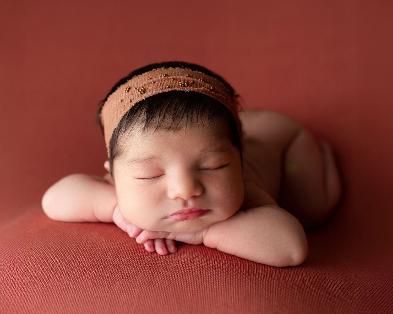 Newborn baby girl sleeping on red backdrop with headband in Vacaville studio