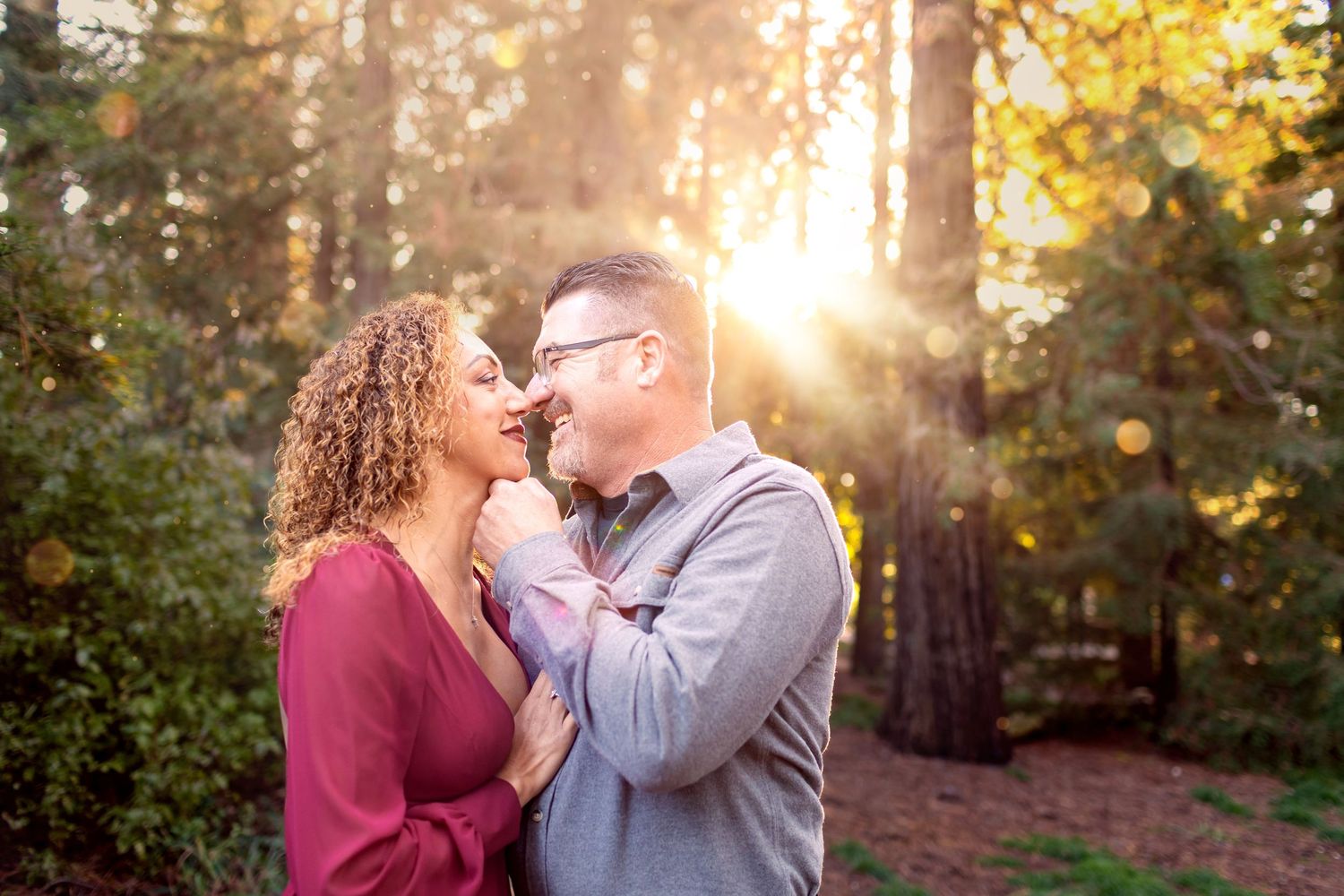 Couple sharing a romantic moment in a sunlit redwood forest, golden light glowing behind them.