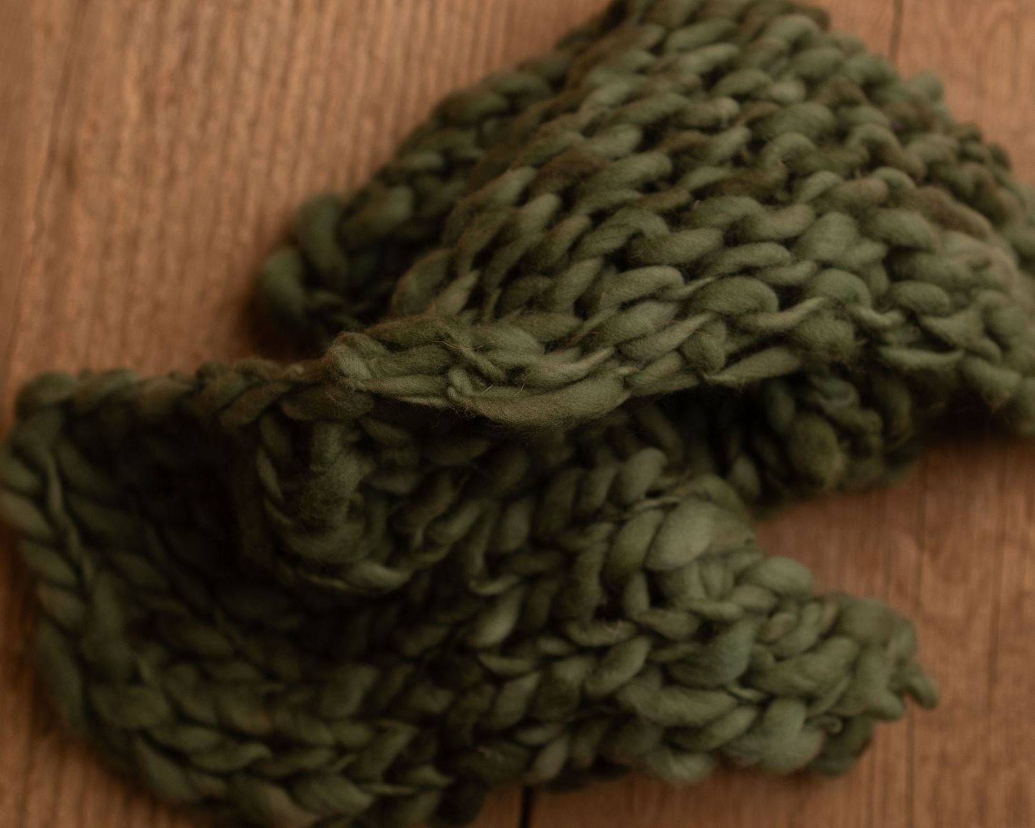 Chunky knit olive green wool yarn swatch with thick stitches on rustic wood surface.