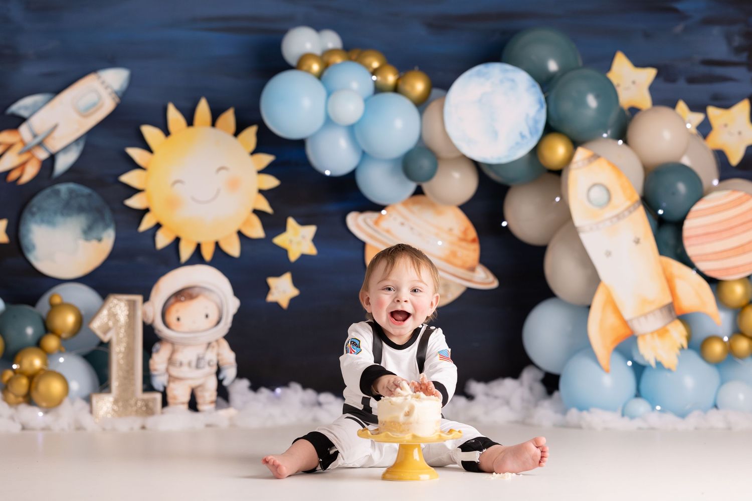 Baby smiling at space-themed first birthday cake smash with astronaut decor, balloons, rockets, and planets on dark blue backdrop.