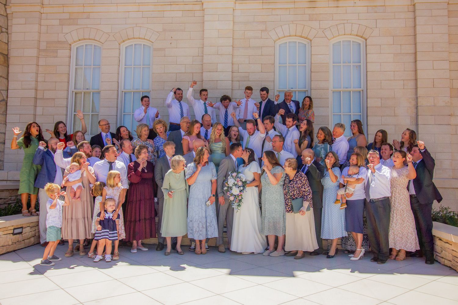Large extended family group photo outside a light stone building after a lds Temple wedding ceremony.