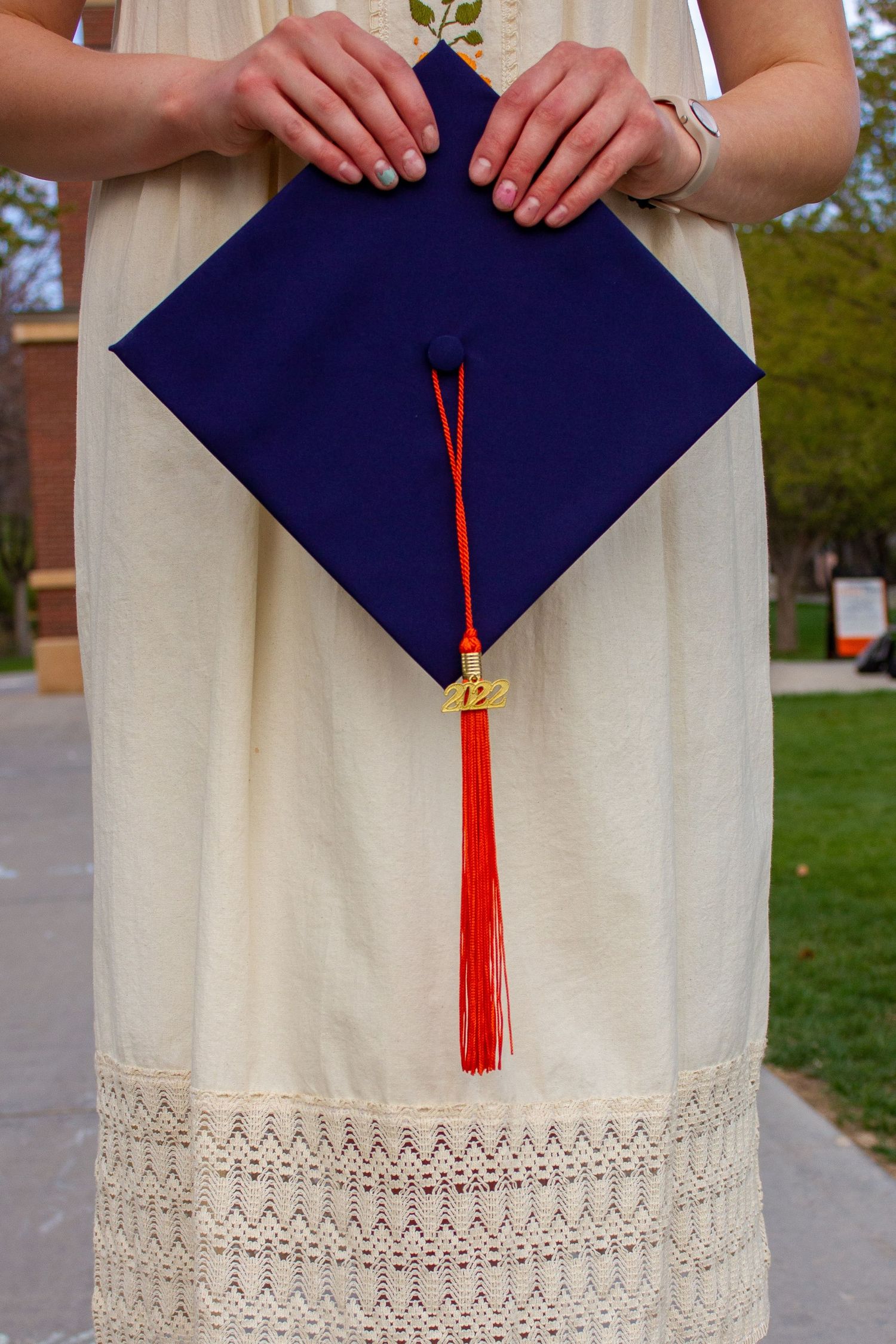 Graduate in white lace dress holding navy blue mortarboard cap with red tassel and 2022 charm.