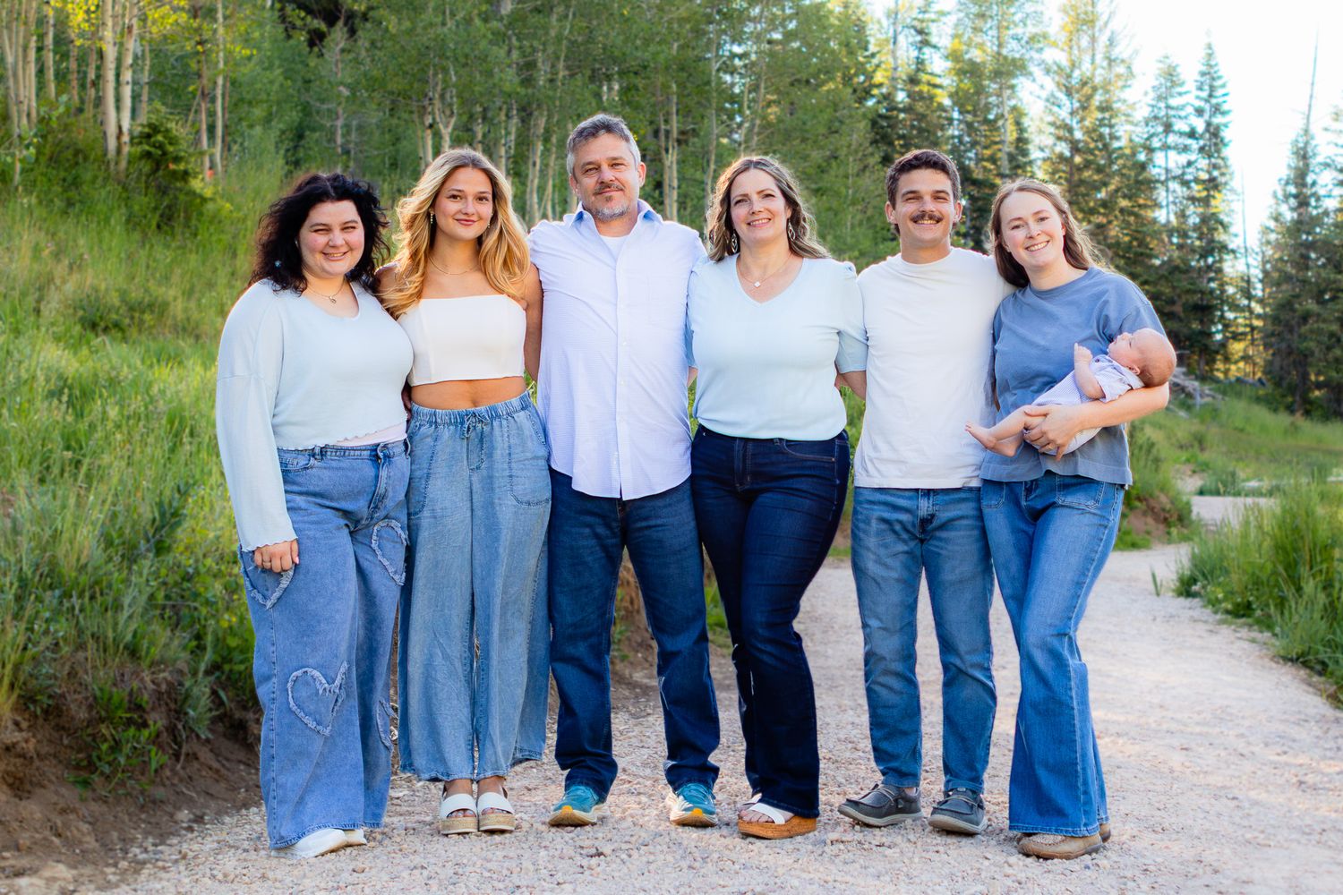 Smiling family of six stands together on a gravel path with lush green forest in the background in Southern Utah.