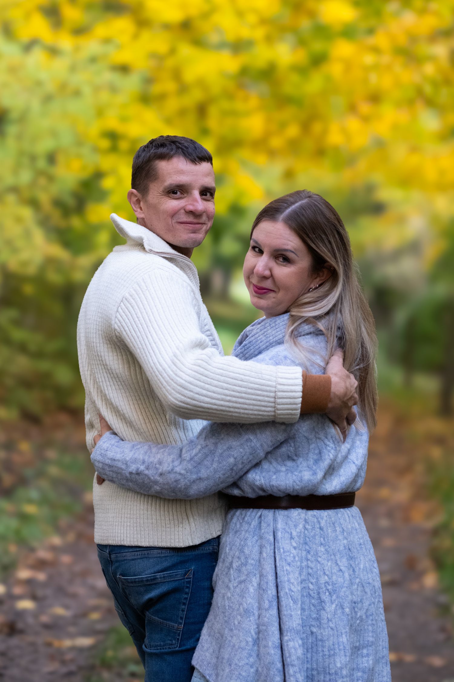 Smiling couple hugging each other on a scenic autumn park path with yellow fall foliage.