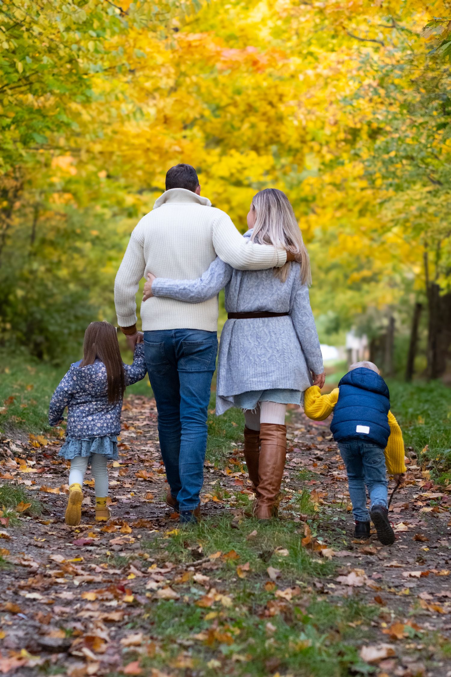 Family walking together through colorful autumn forest path from behind.