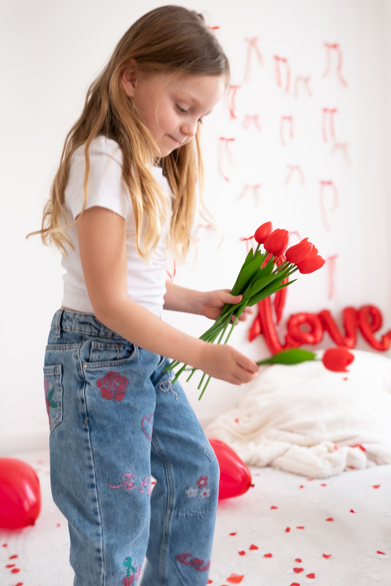 Young blonde girl holding red tulips in a Valentine's Day decorated room with love sign.