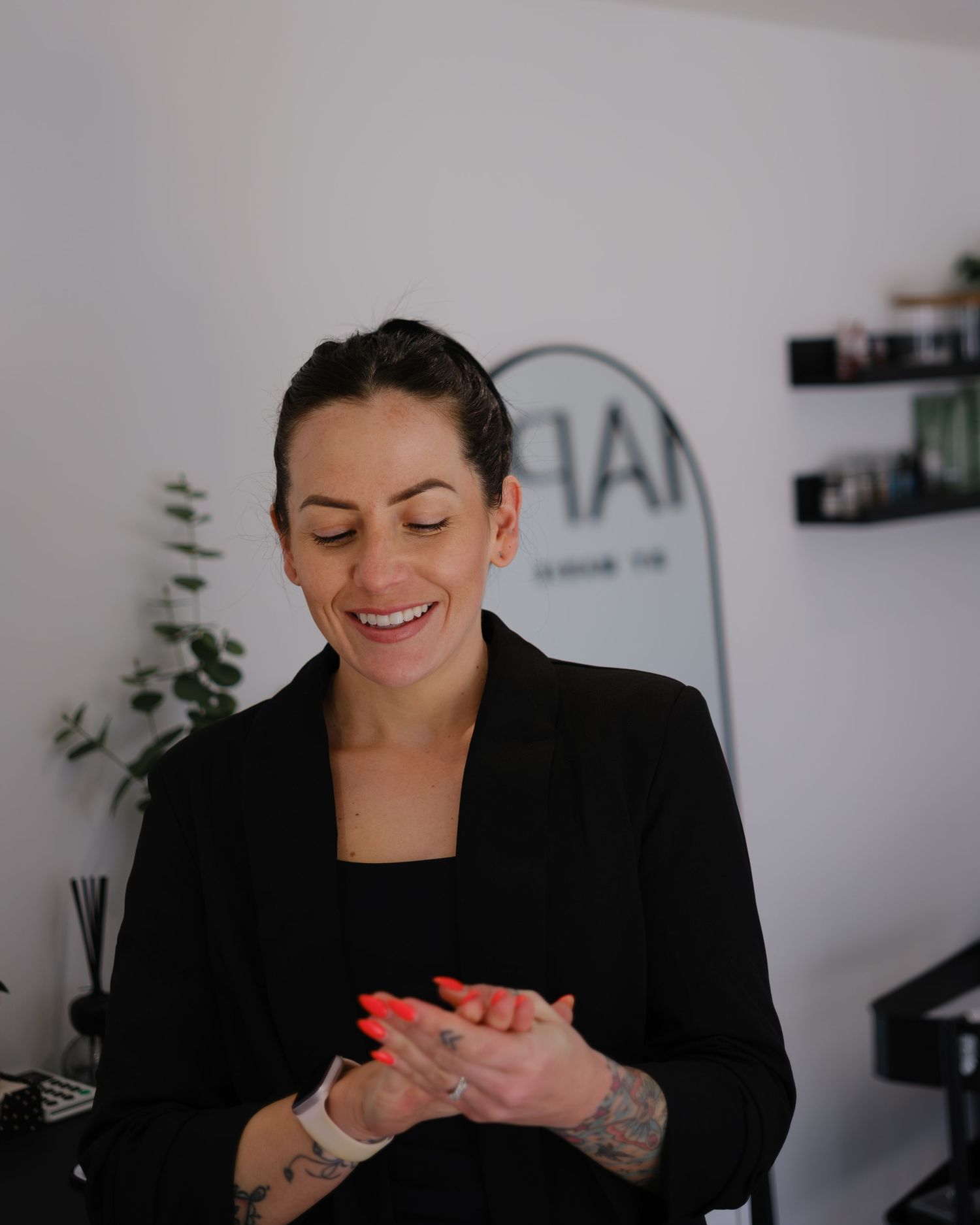 Smiling female brow artist with tattoos and red nails at Shaped by Marie salon.
