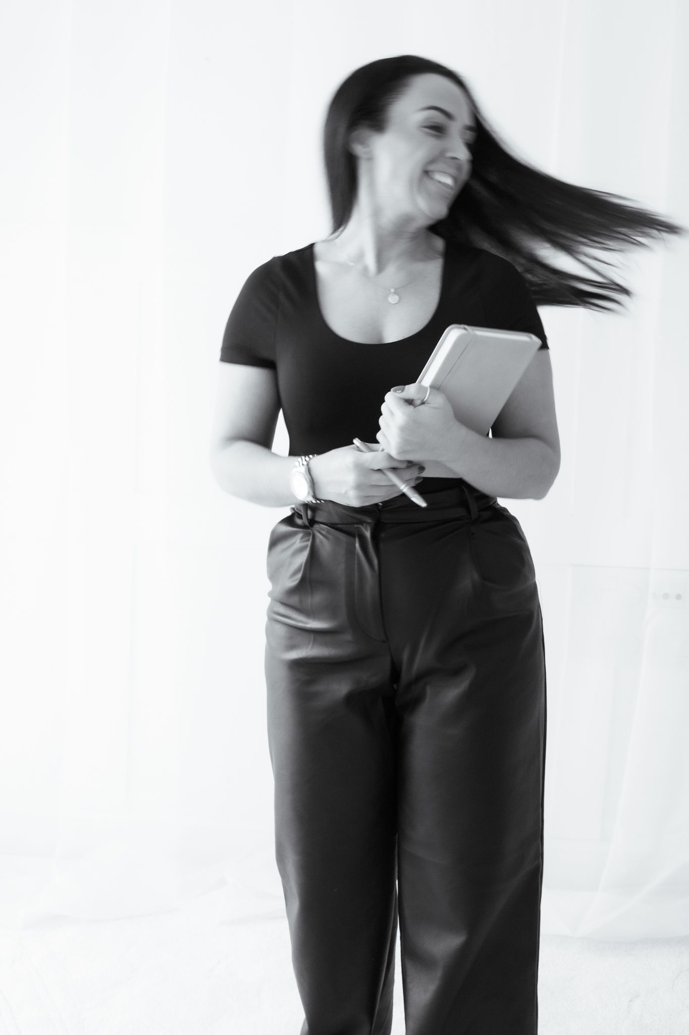 Black and white photo of smiling woman with flowing hair holding notebook.