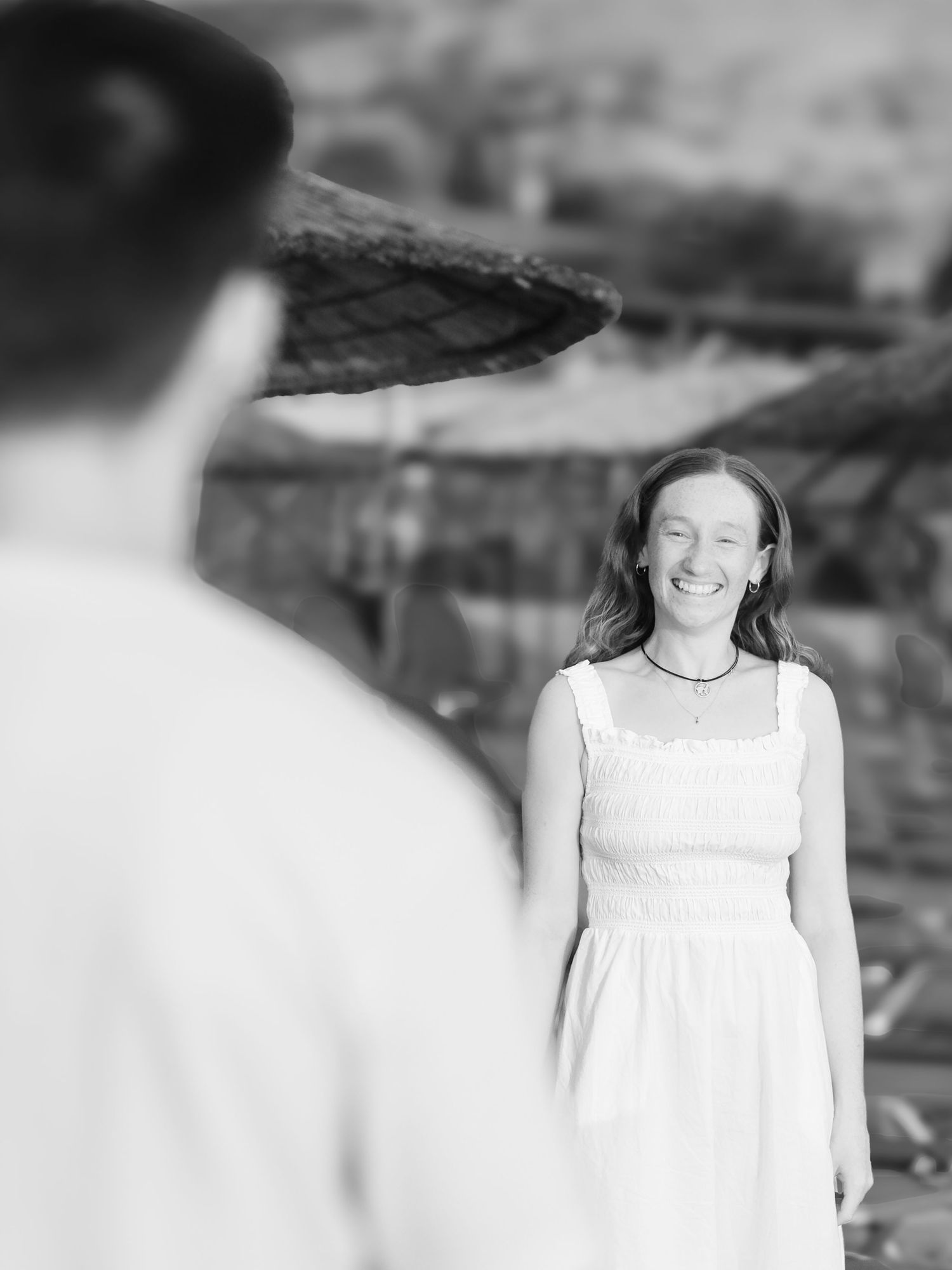 Black and white portrait of a smiling young woman in a white dress laughing outdoors at a beach resort.