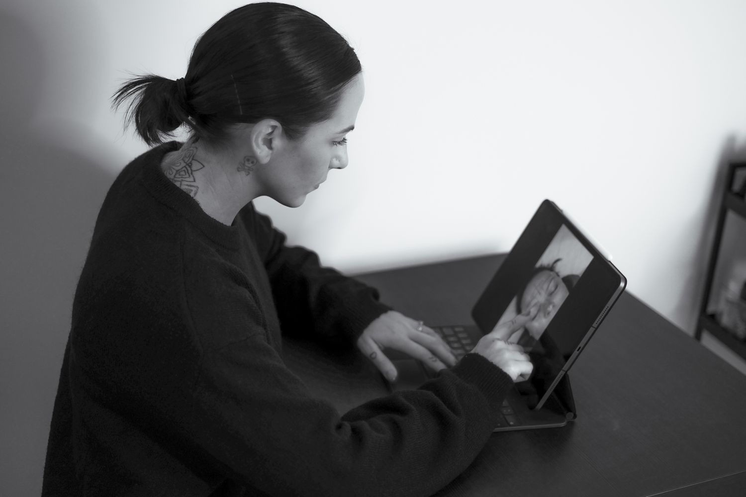 Black and white photo of a woman having a video call on a tablet at a desk.