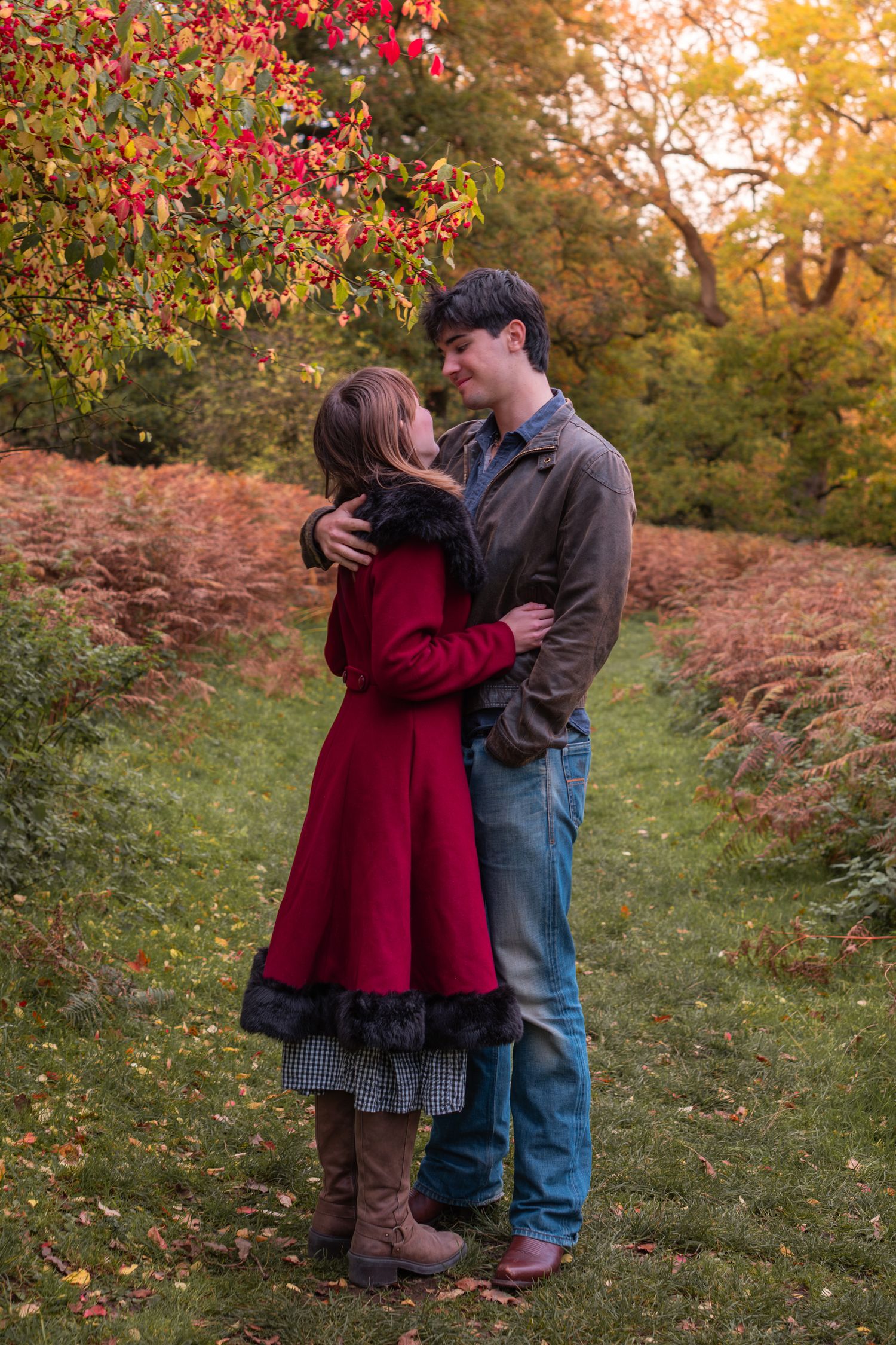 Romantic couple embracing in autumn park, woman in red coat and man in brown jacket surrounded by fall foliage.