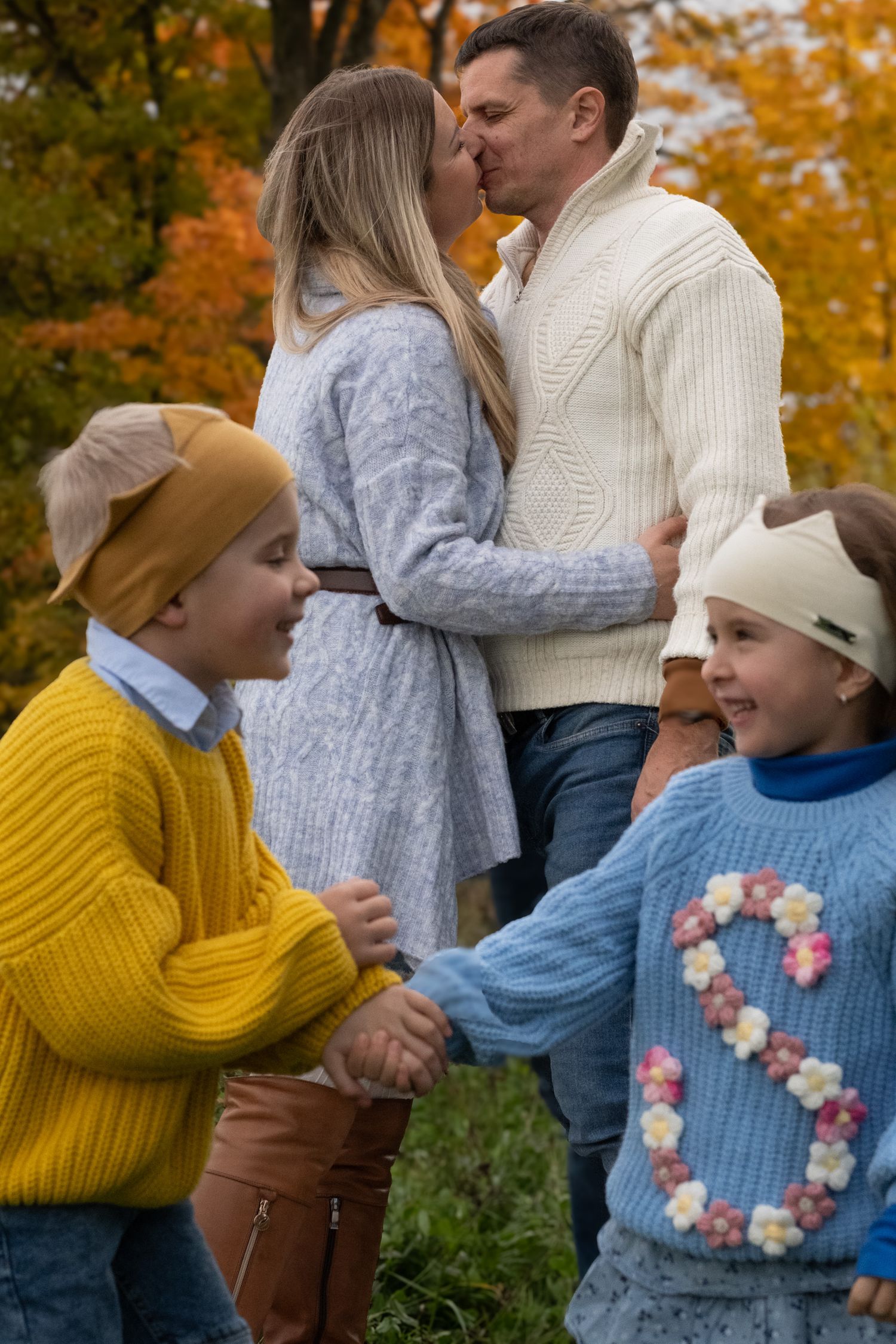 Family with two children sharing kiss in vibrant autumn park setting.