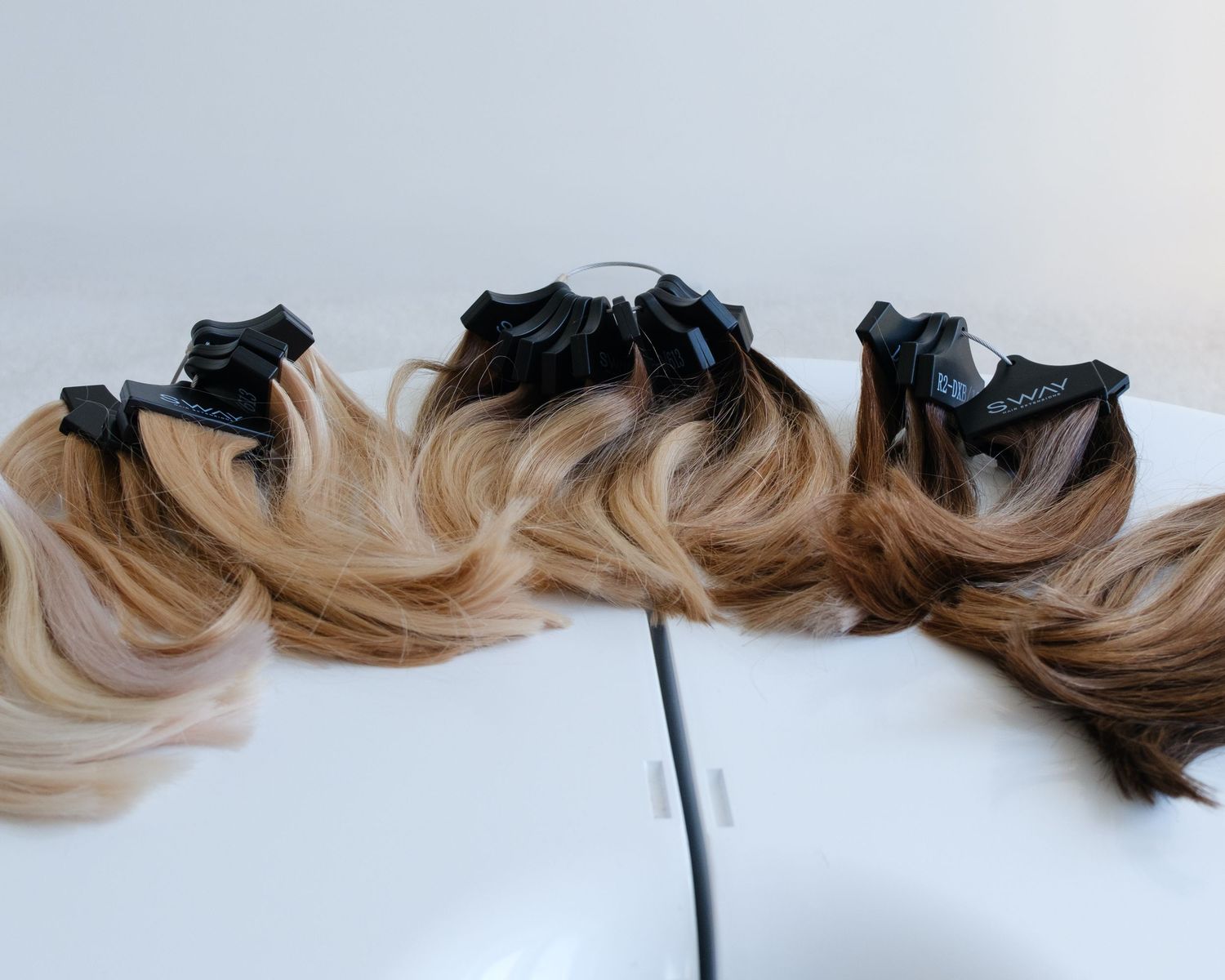 Three sections of ombre hair extensions ranging from dark brown to blonde roots clipped on a white surface.