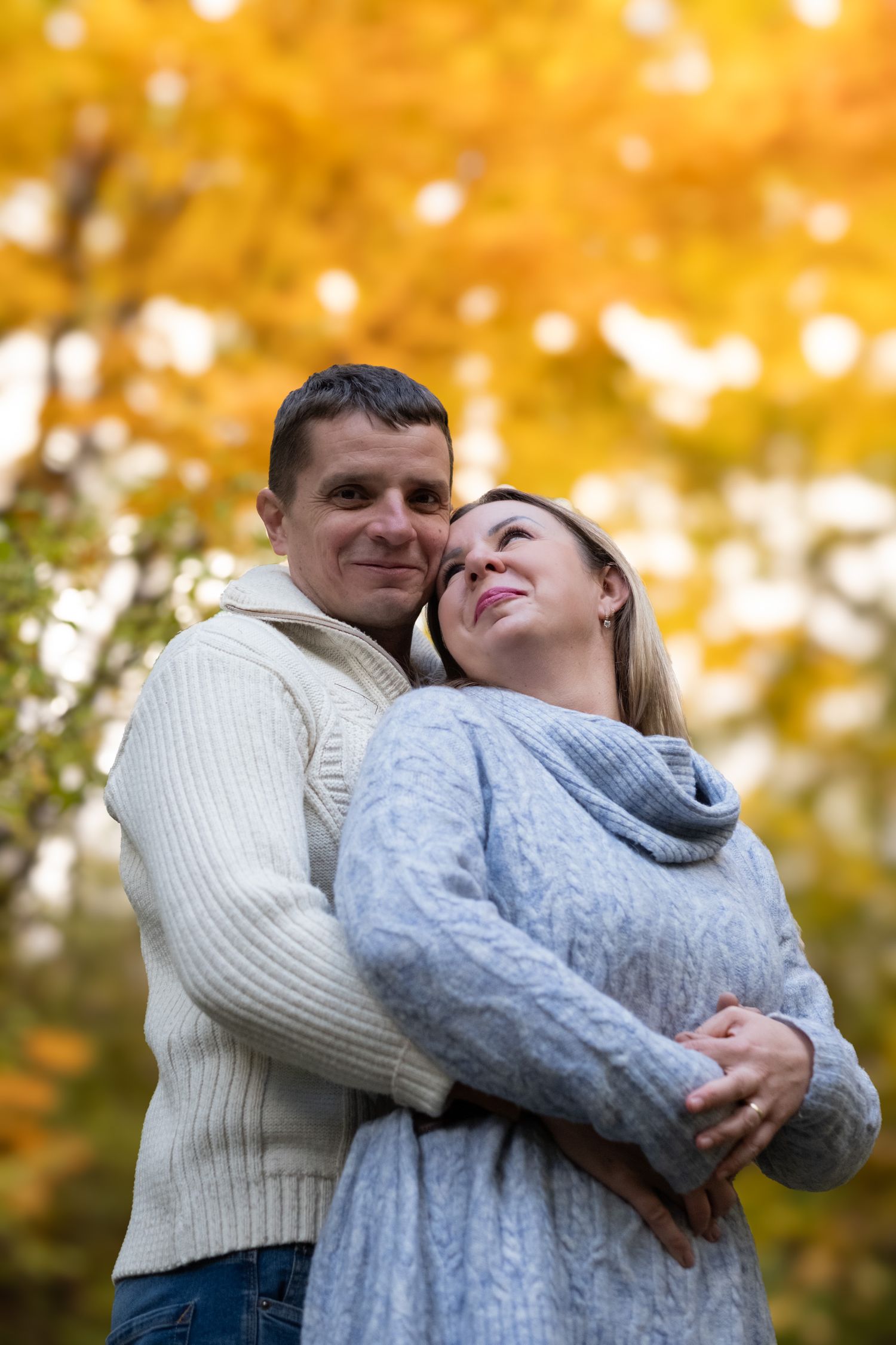 Loving couple embracing warmly in an autumn park with golden yellow foliage in background.