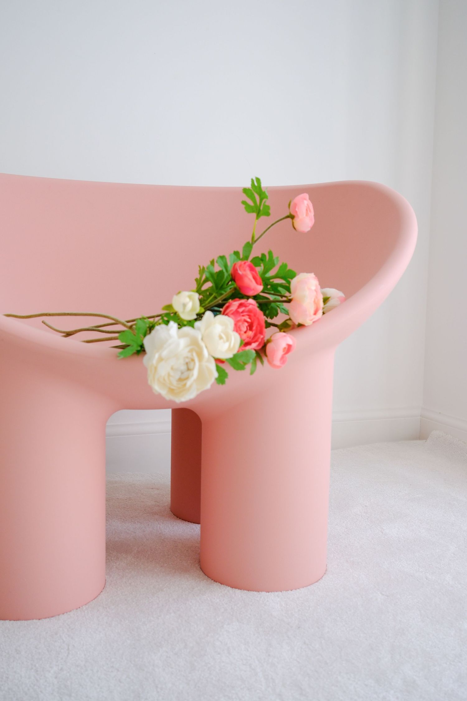 A modern pink curved sofa adorned with colorful white and pink roses against a white wall.