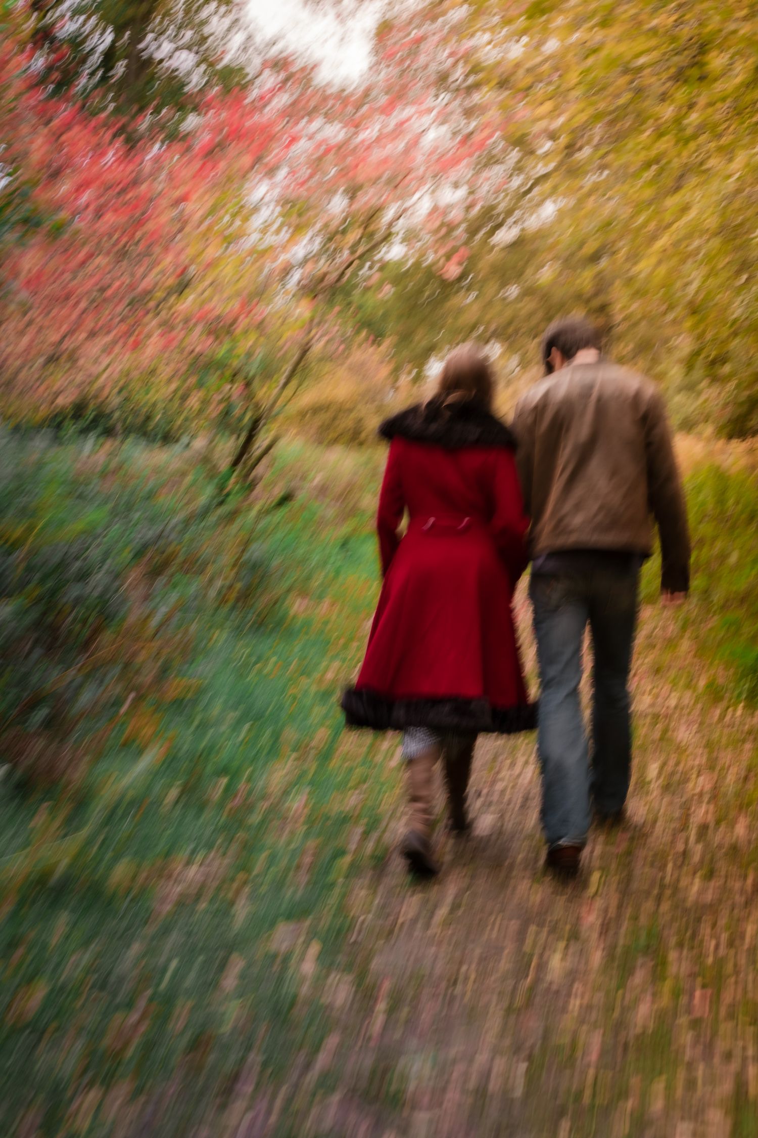 A couple walks arm in arm along a colorful autumn path, captured with a radial blur effect.