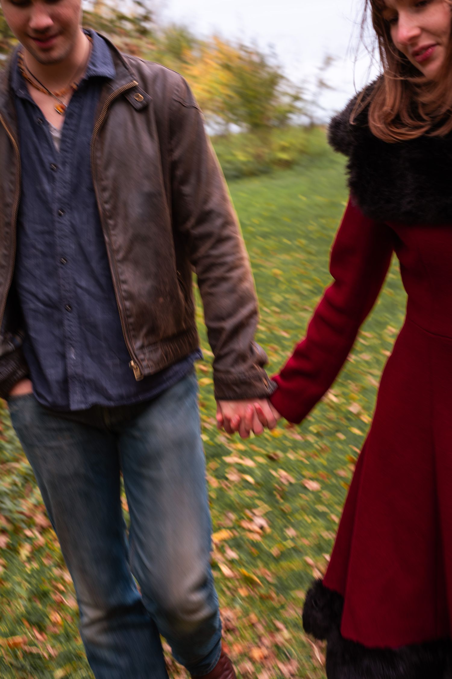 A couple holds hands while walking through an autumn park, captured with a motion blur effect.