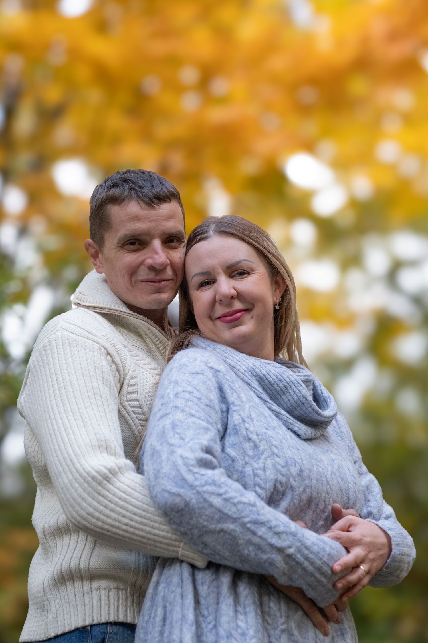 Affectionate couple posing together in autumn park with warm golden yellow leaves in background.