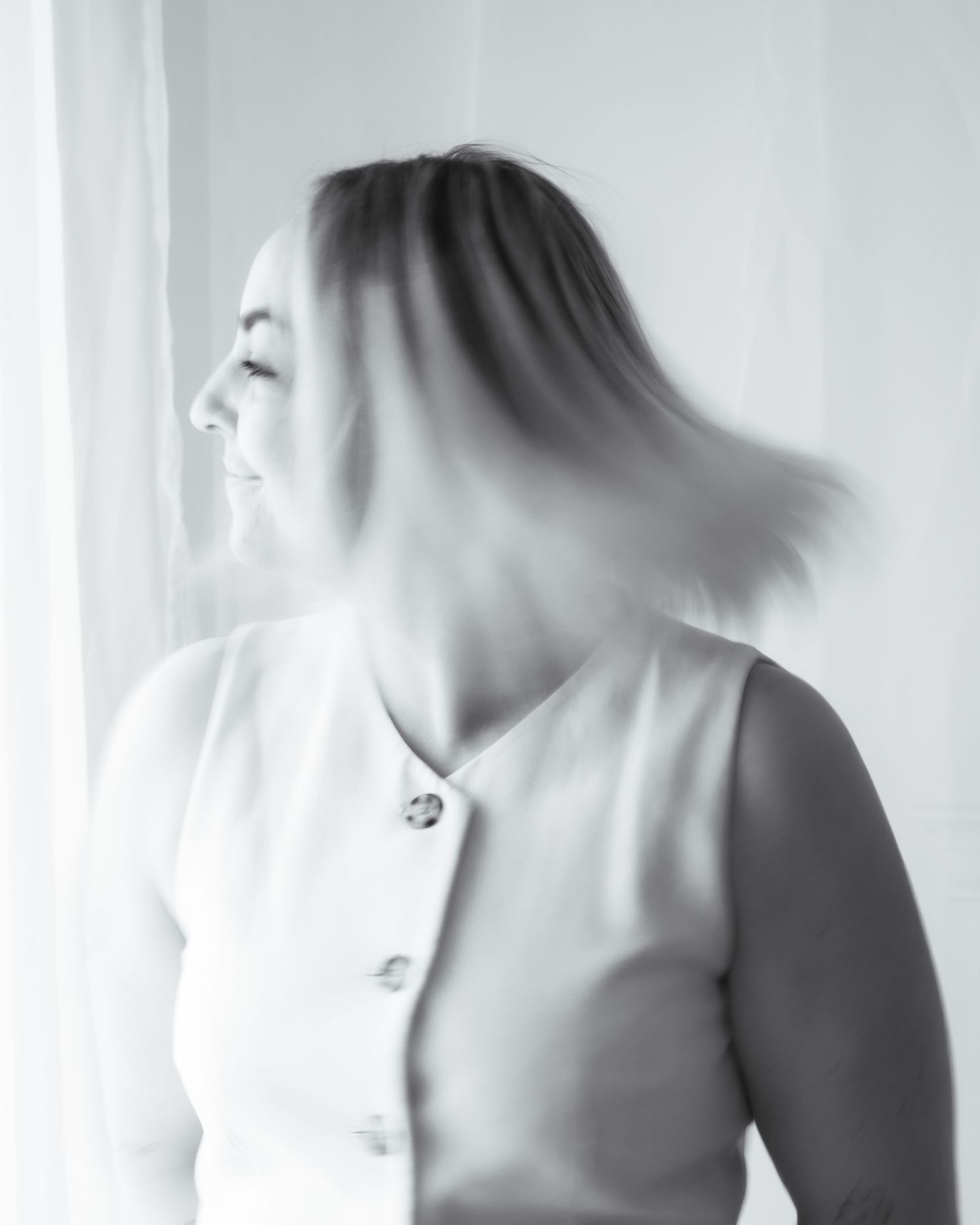 Black and white motion blur portrait of woman in sleeveless button vest tossing her hair.