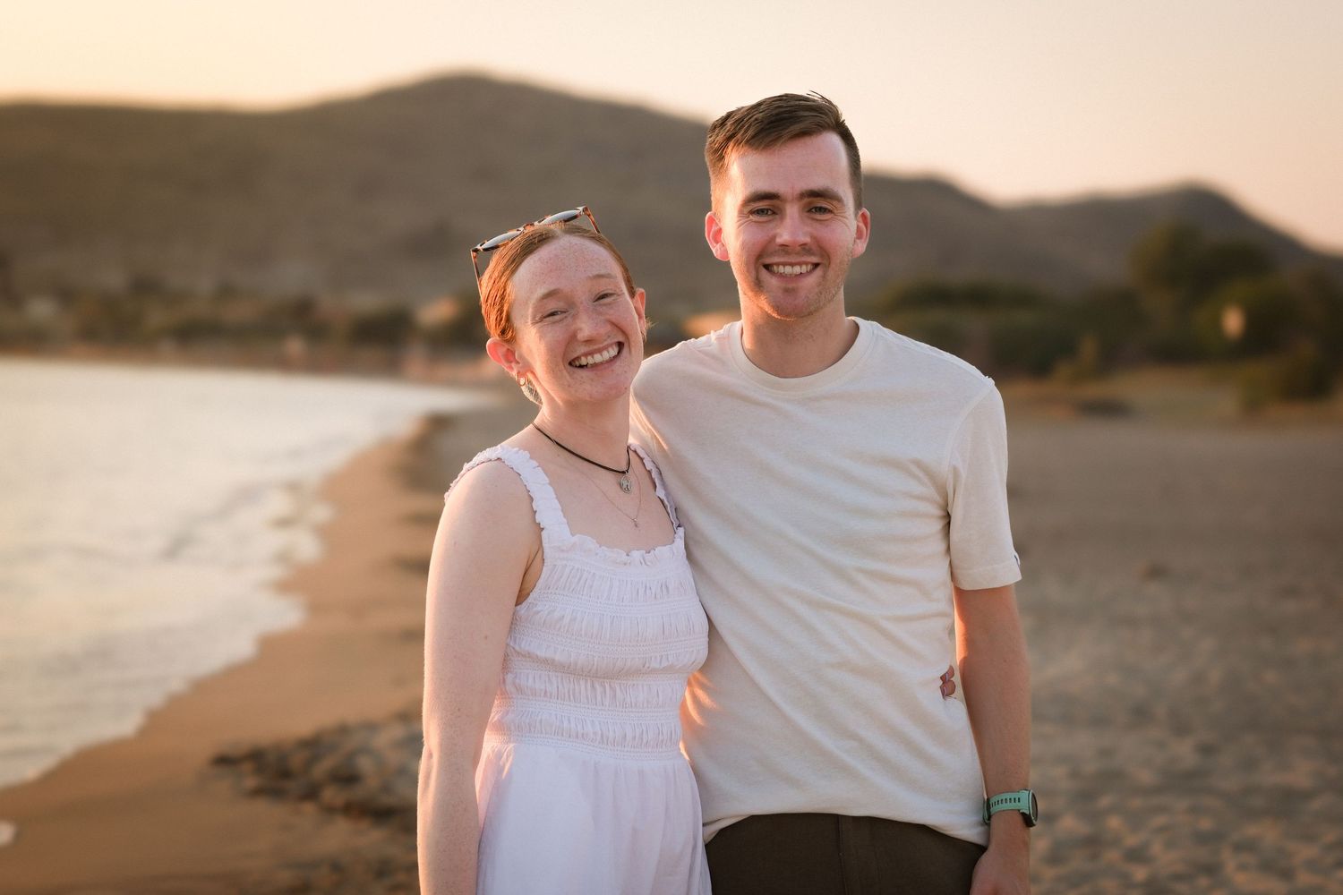 Happy young couple embracing and smiling together on a sandy beach at golden sunset hour.