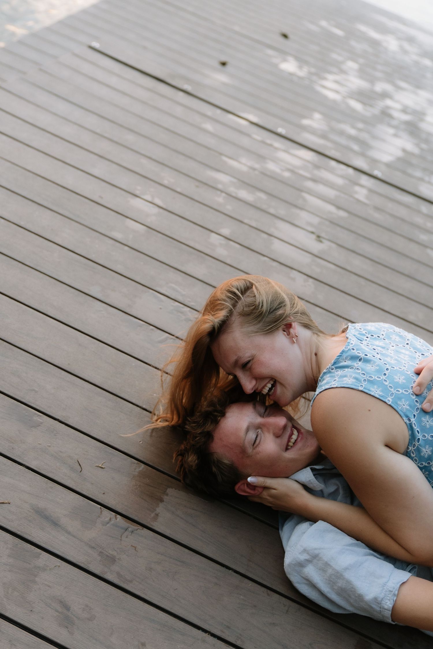 Two young women laughing and lying together on a wooden deck, sharing a joyful moment.