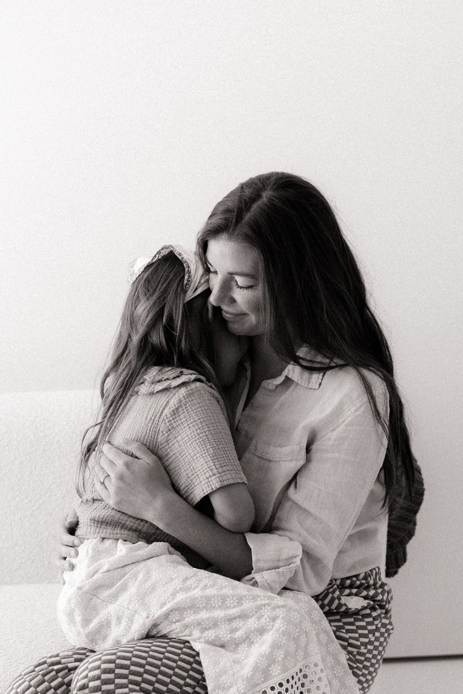Black and white photo of a mother tenderly embracing her young daughter while seated together.