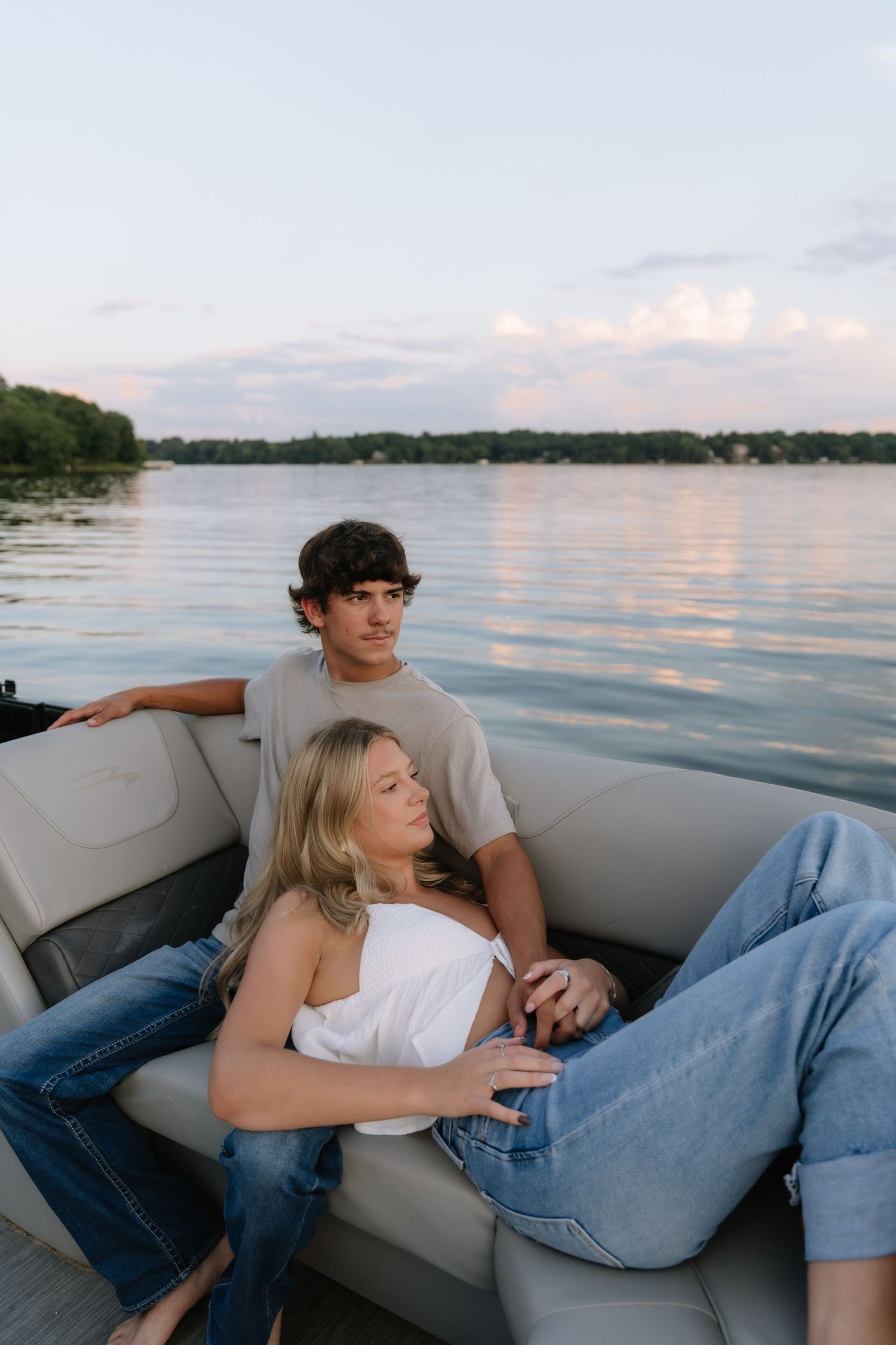 A young couple relaxing on a pontoon boat at sunset on a calm lake, woman in white top and jeans.