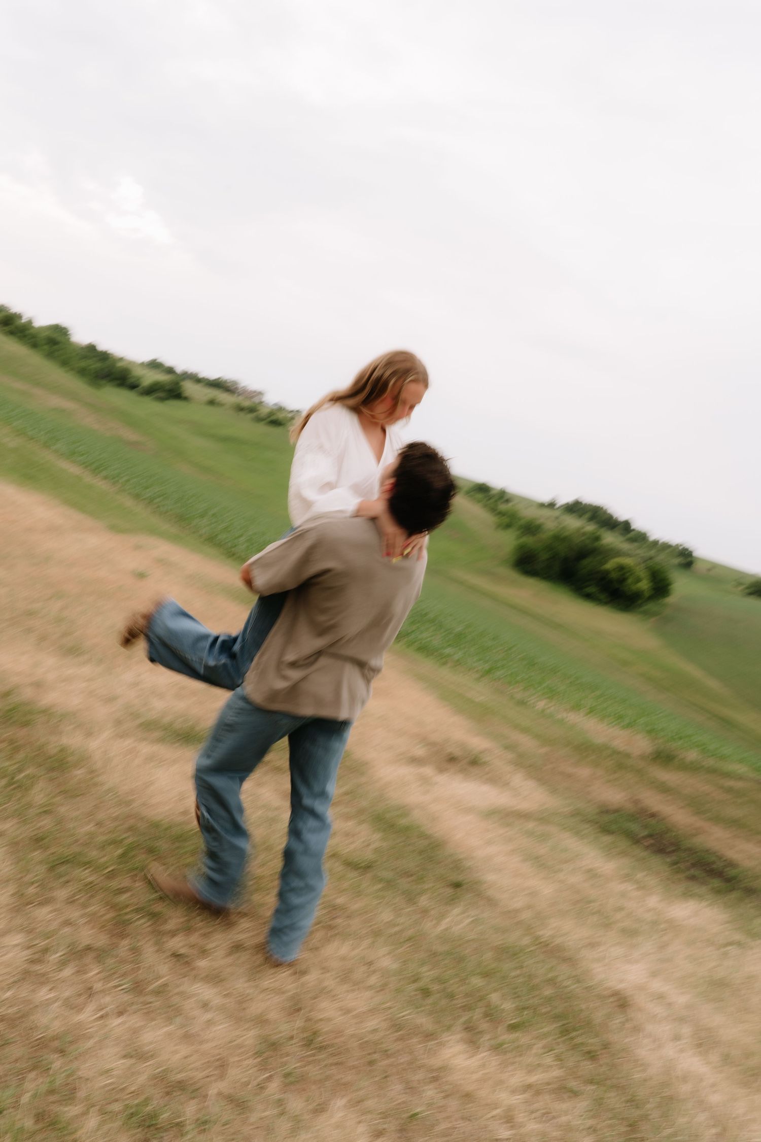 A man lifts a woman in a field, sharing a romantic moment in a blurred motion photo outdoors.