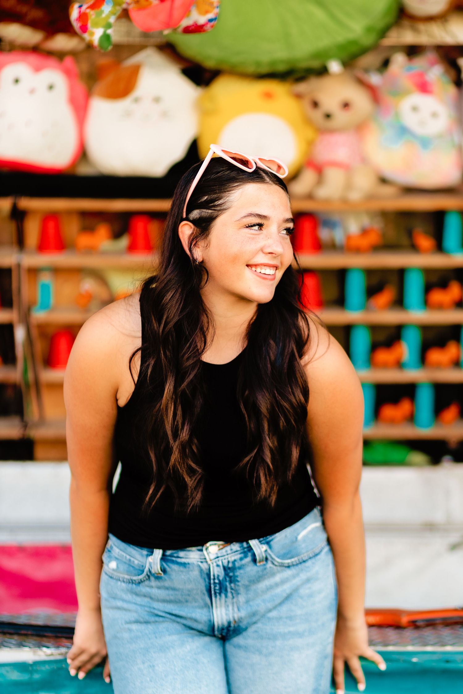 Smiling young woman in black tank top with sunglasses on head at a carnival prize booth.