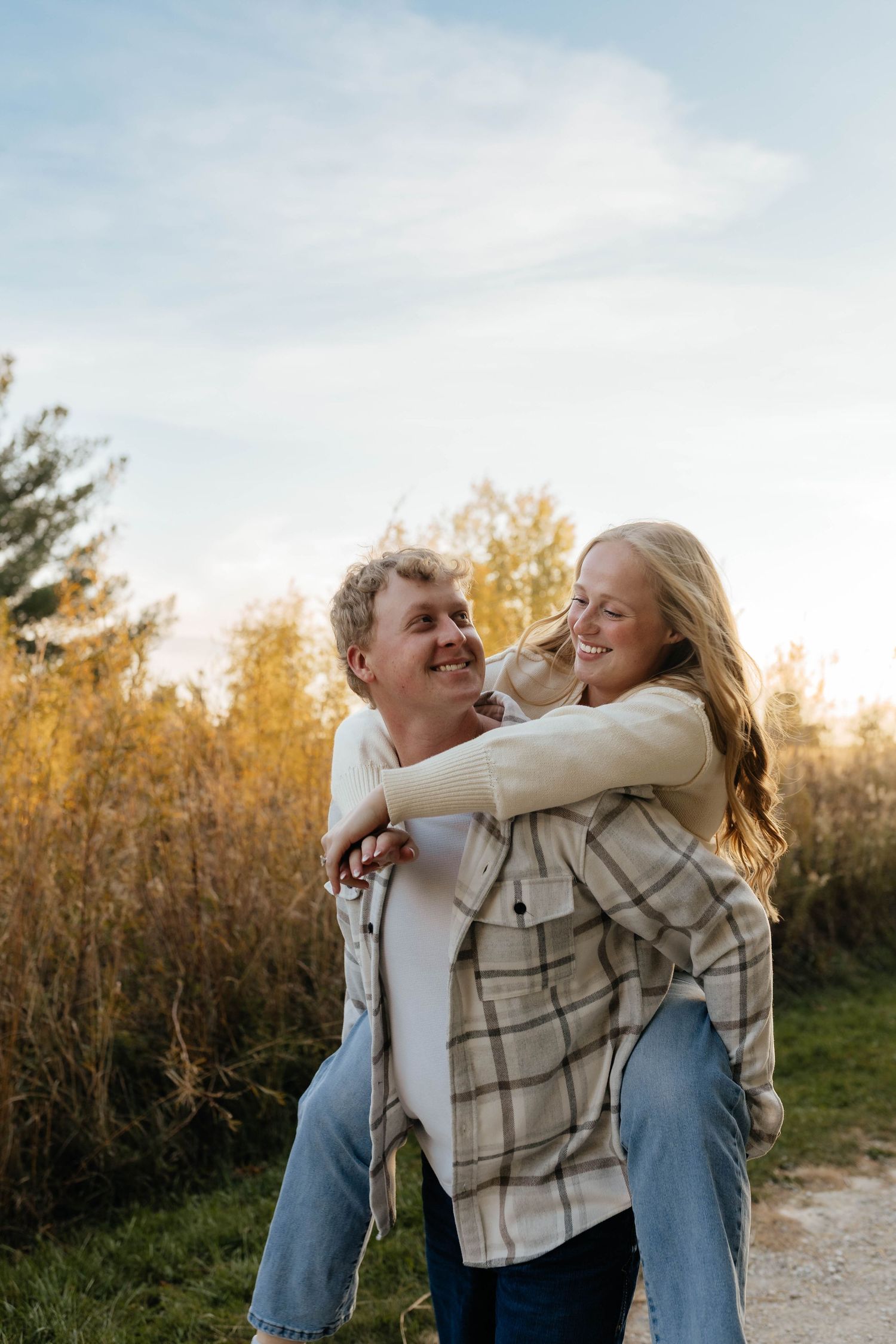 A happy couple shares a piggyback ride outdoors among golden autumn foliage.