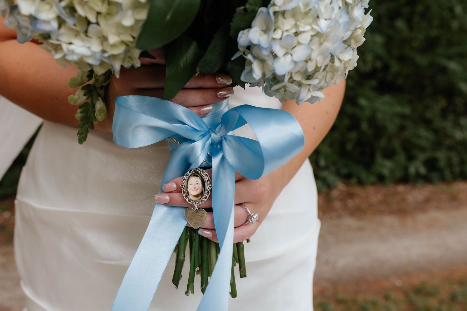 Close-up of bridal bouquet with white roses and blue hydrangeas tied with light blue satin ribbon.