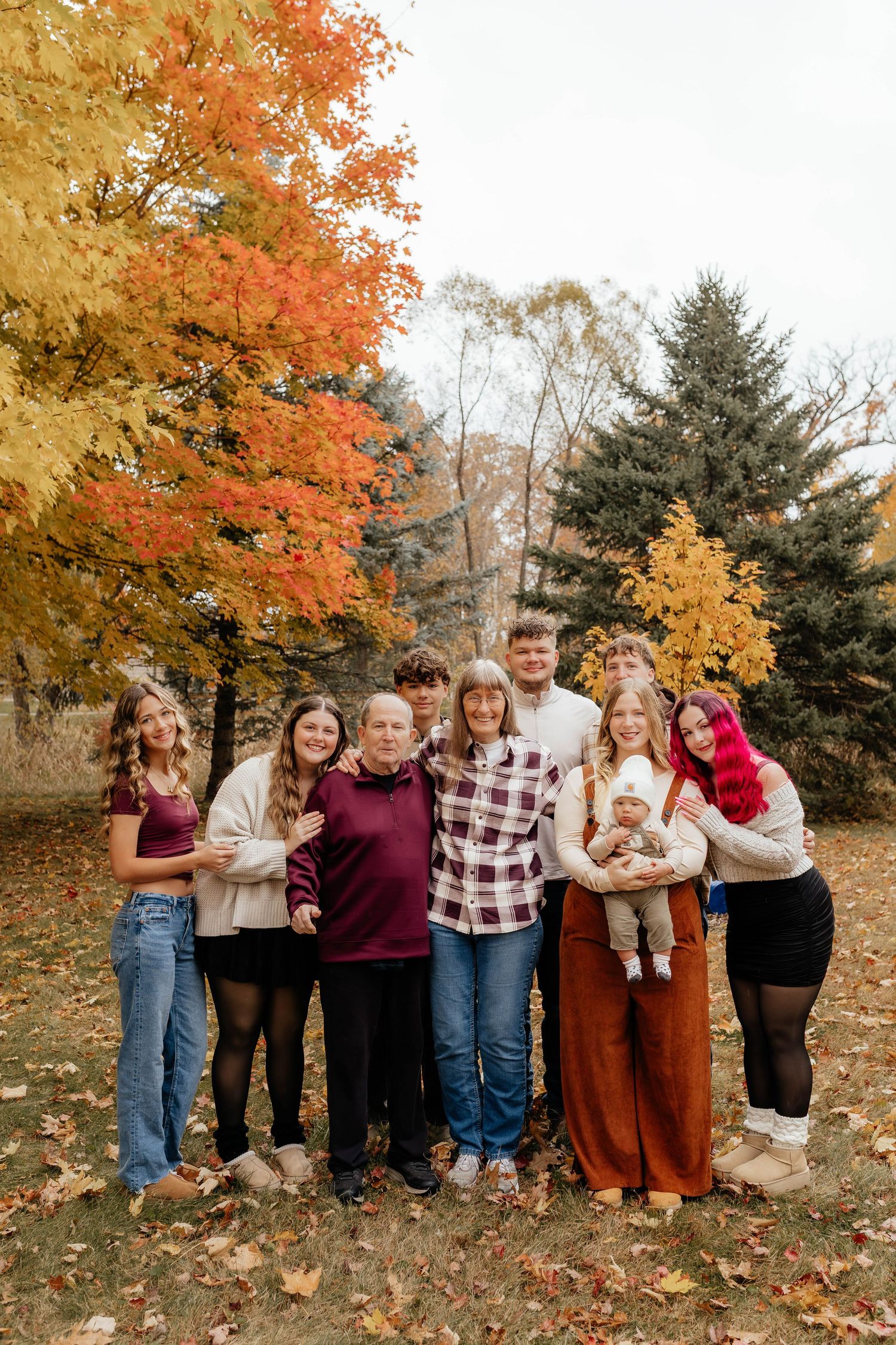 Family of eight posing outdoors among vibrant fall foliage with orange and yellow trees in background.