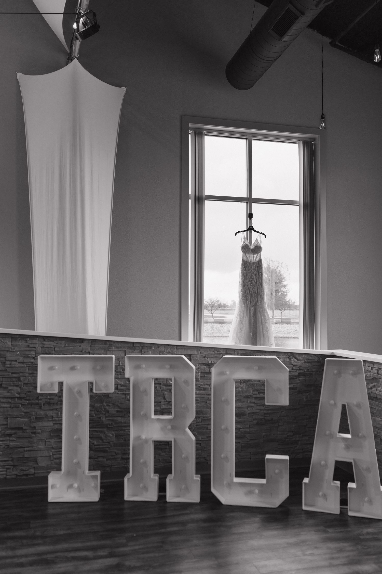 Black and white photo of illuminated TRCA marquee letters with a wedding dress hanging in a window above.
