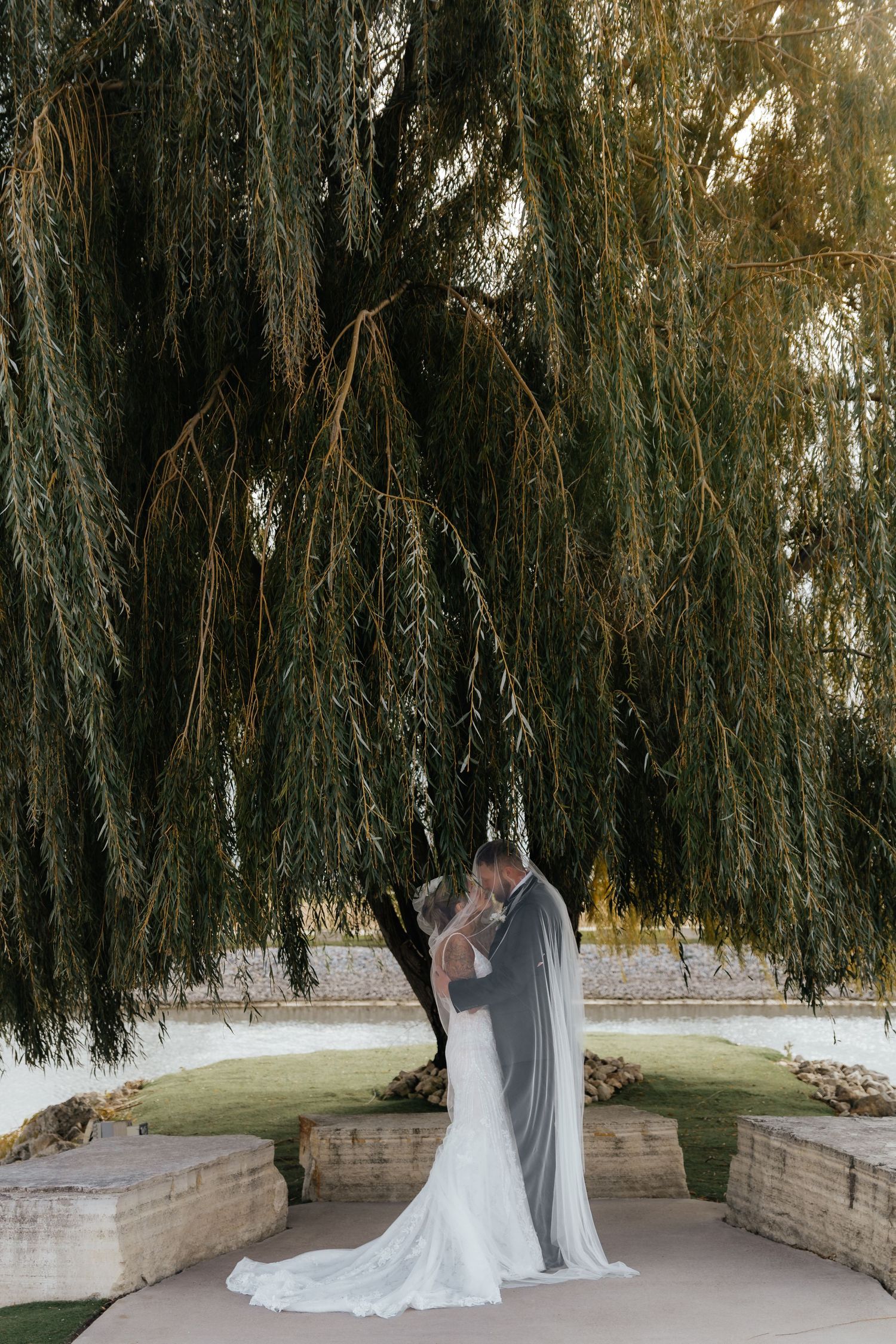 Bride and groom sharing a romantic moment under a weeping willow tree at golden hour.