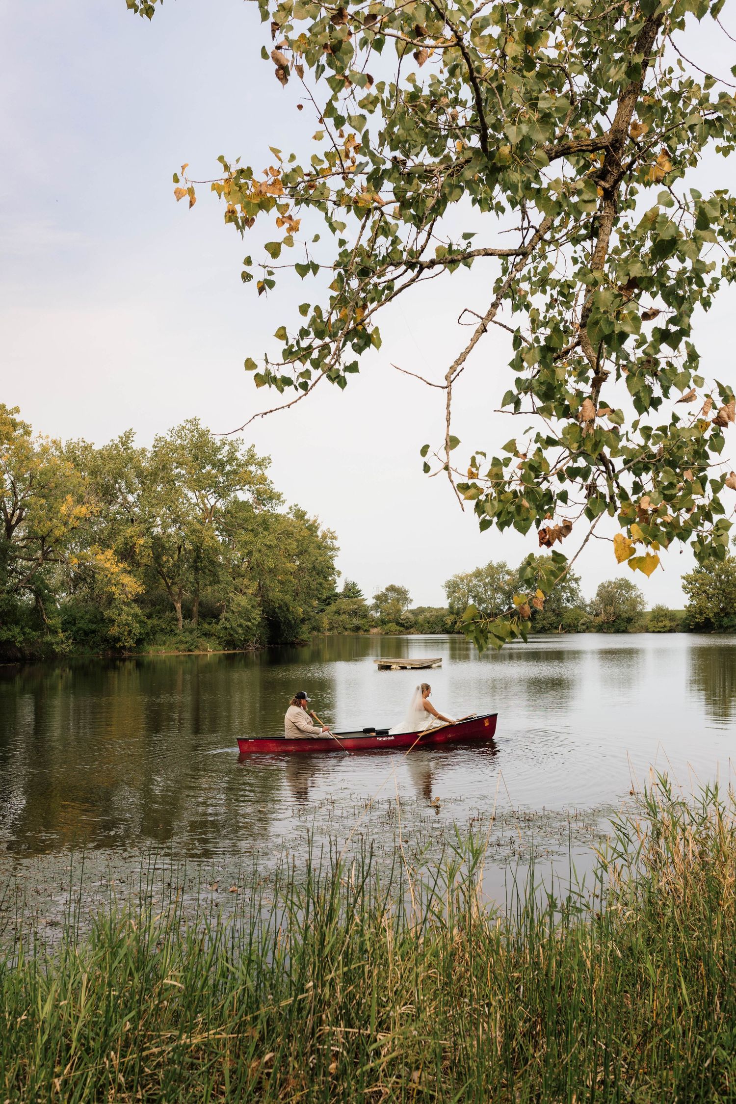 Couple rowing a red canoe on a peaceful lake surrounded by lush autumn trees.