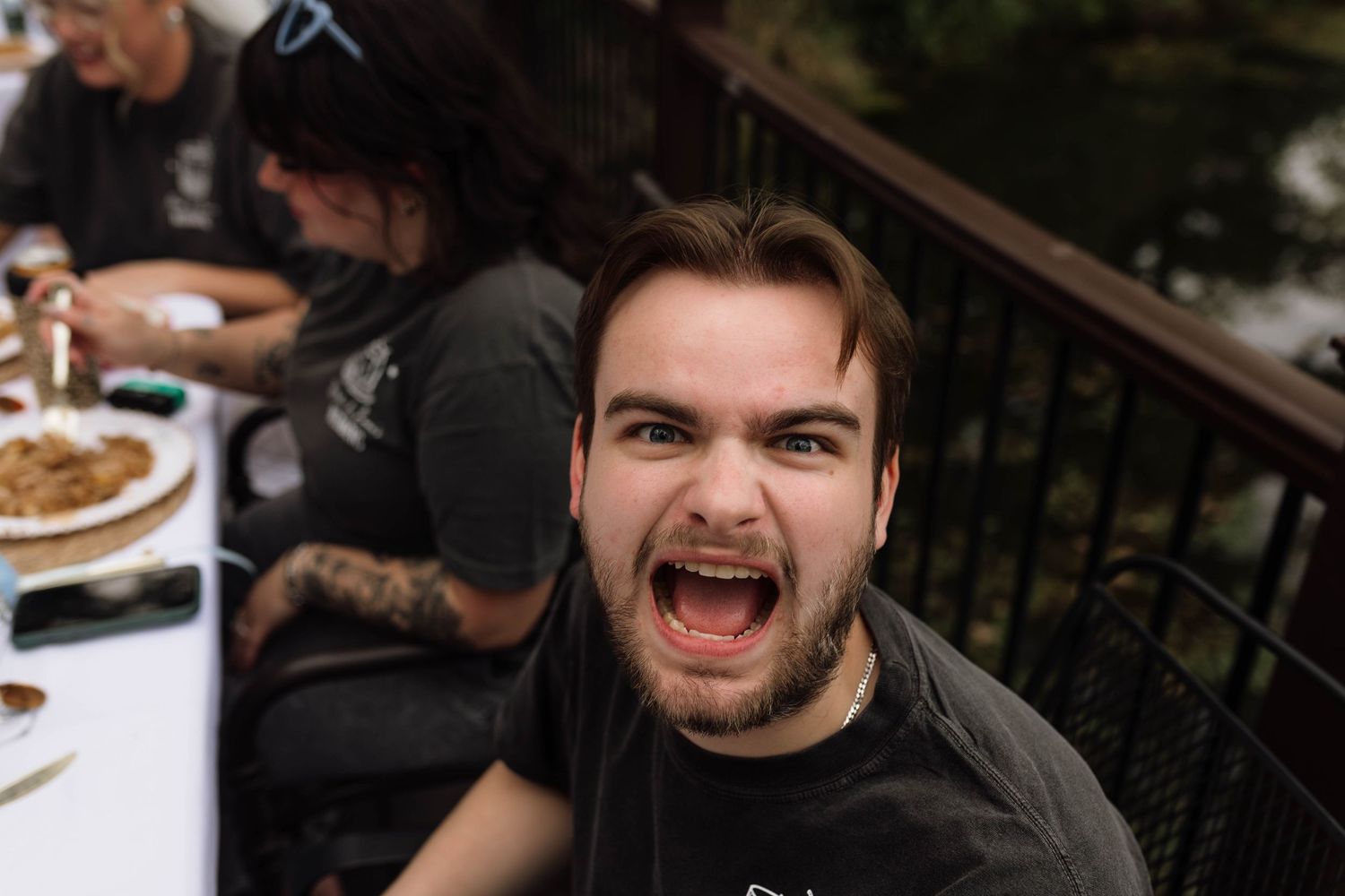 Young man making a funny face at the camera during an outdoor wedding reception dinner.