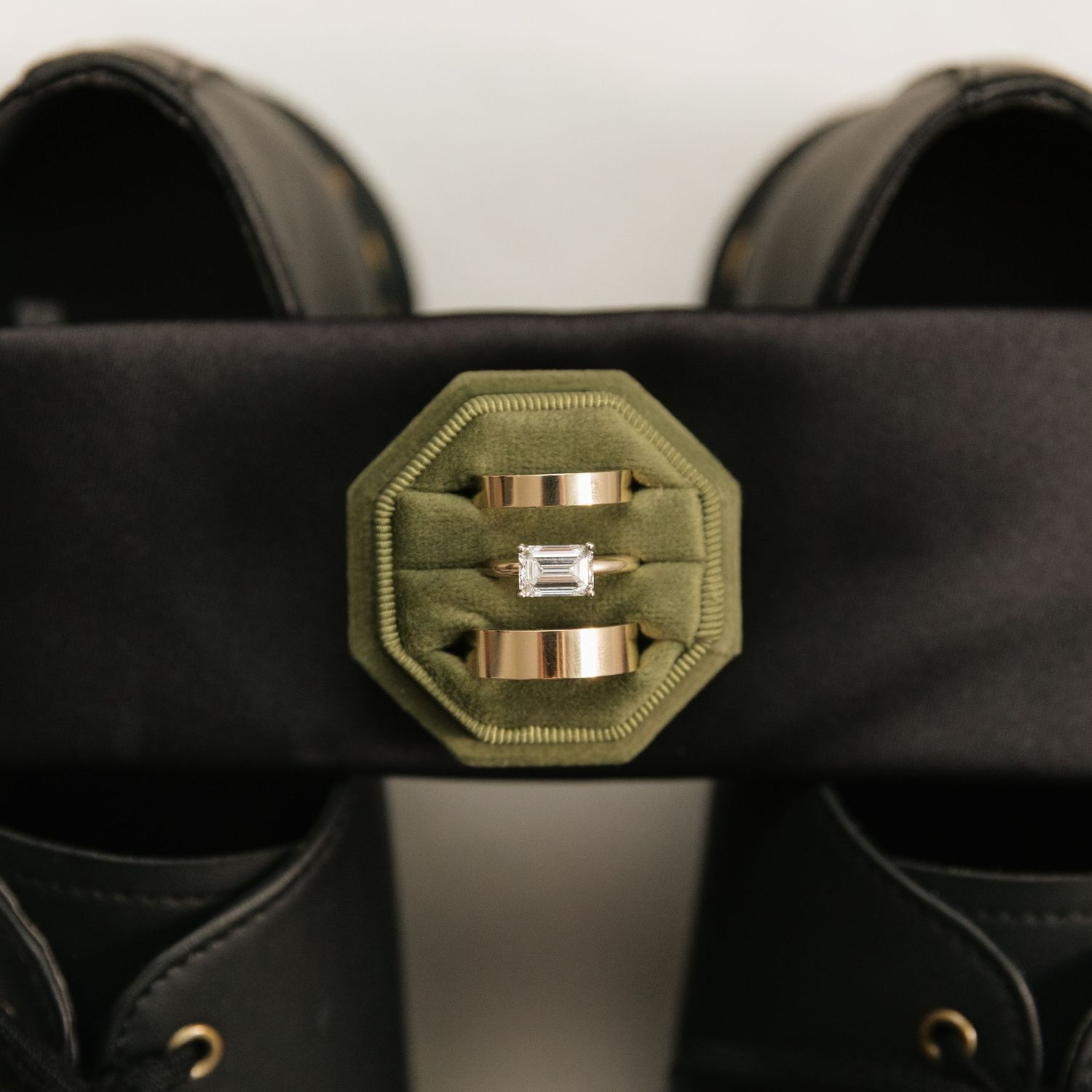 Two rose gold wedding bands and diamond engagement ring in green octagonal velvet ring box on black shoes.